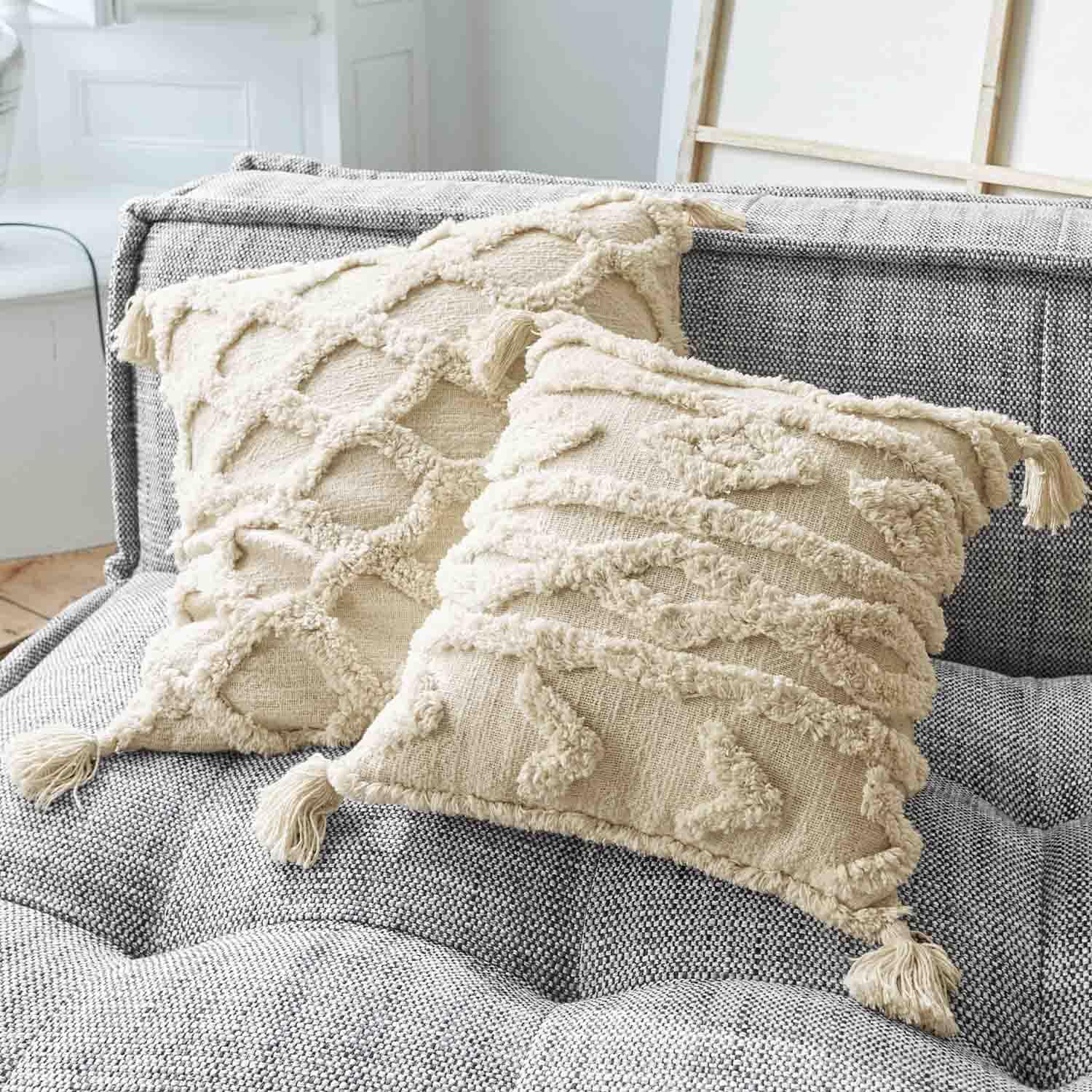 Cojines decorativos beige de algodón con borlas sobre sofá gris, textura y diseño tejido