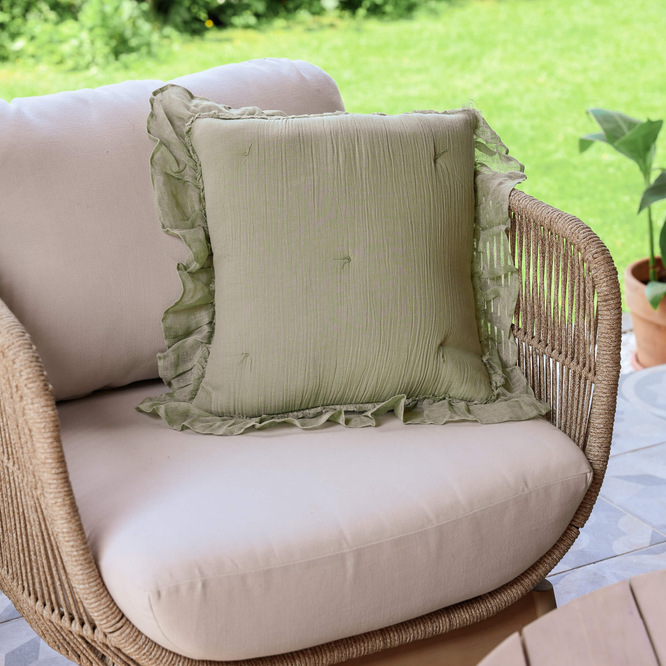 Cojín decorativo verde de lino con volante sobre sofá beige de ratán en terraza