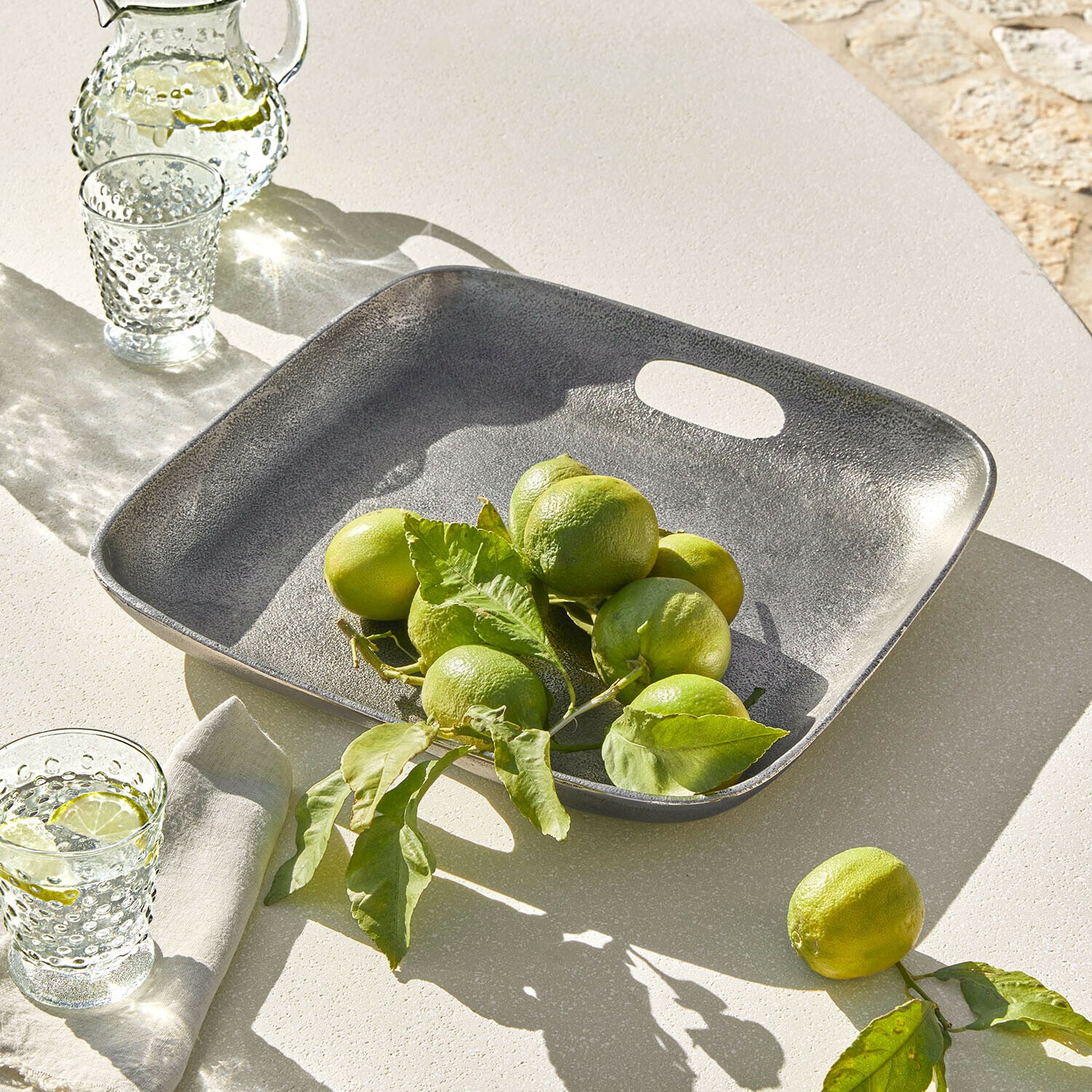 Bandeja Tarevo Bandeja cuadrada de metal gris con limones verdes sobre mesa clara, decoración de mesa veraniega
