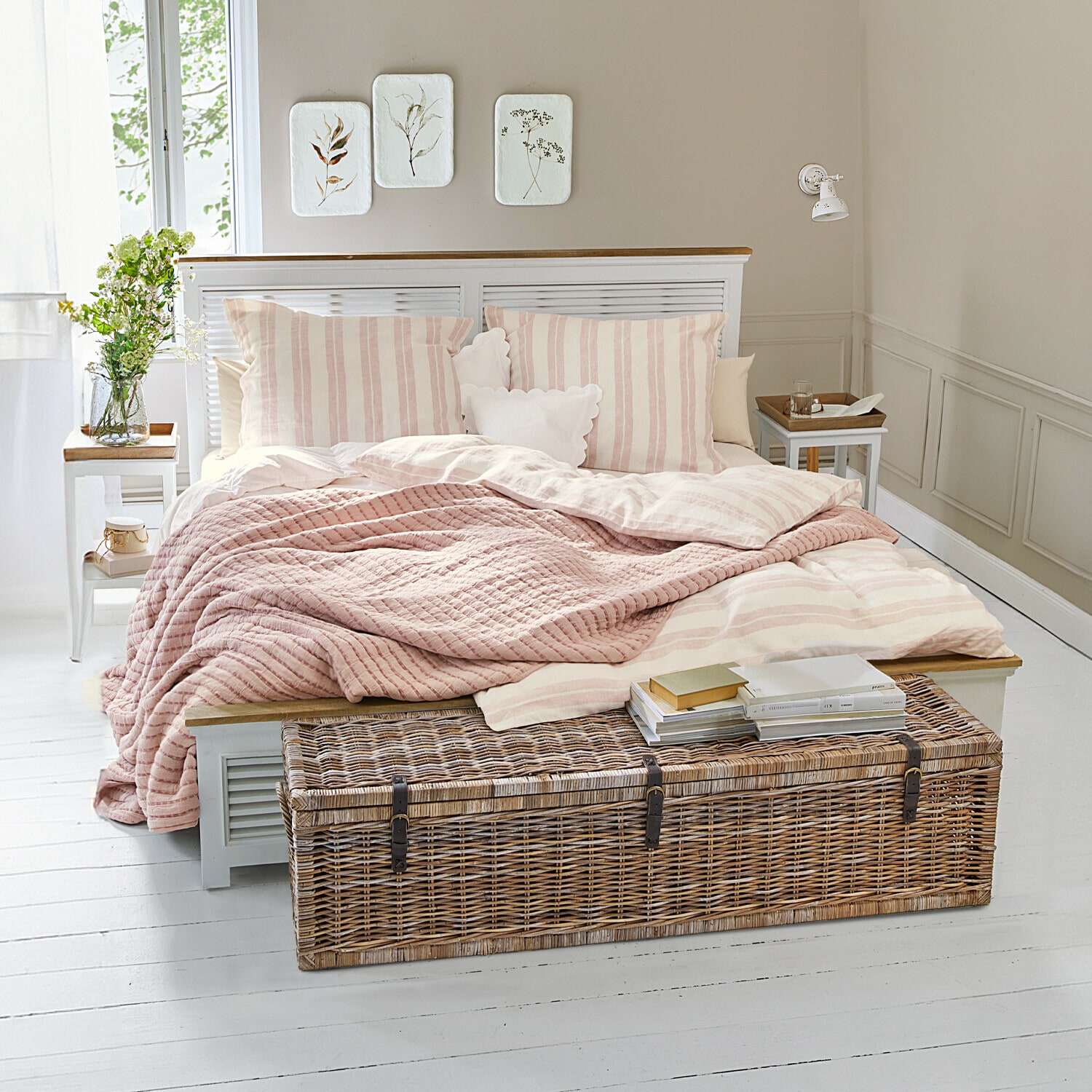 Dormitorio acogedor con cama de rayas rosa claro y baúl de mimbre sobre suelo blanco