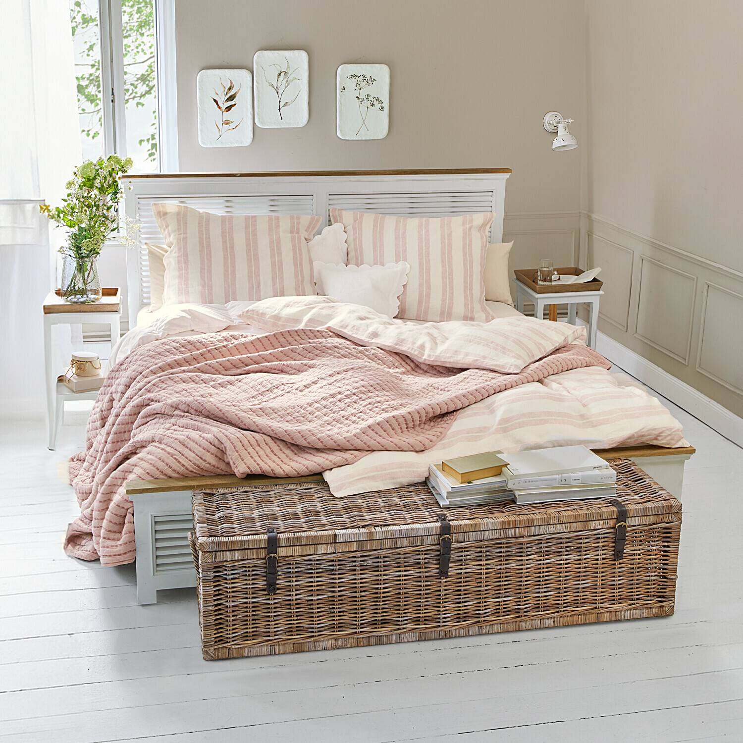 Cama Antje Dormitorio acogedor con cama de rayas rosa claro y baúl de mimbre sobre suelo blanco