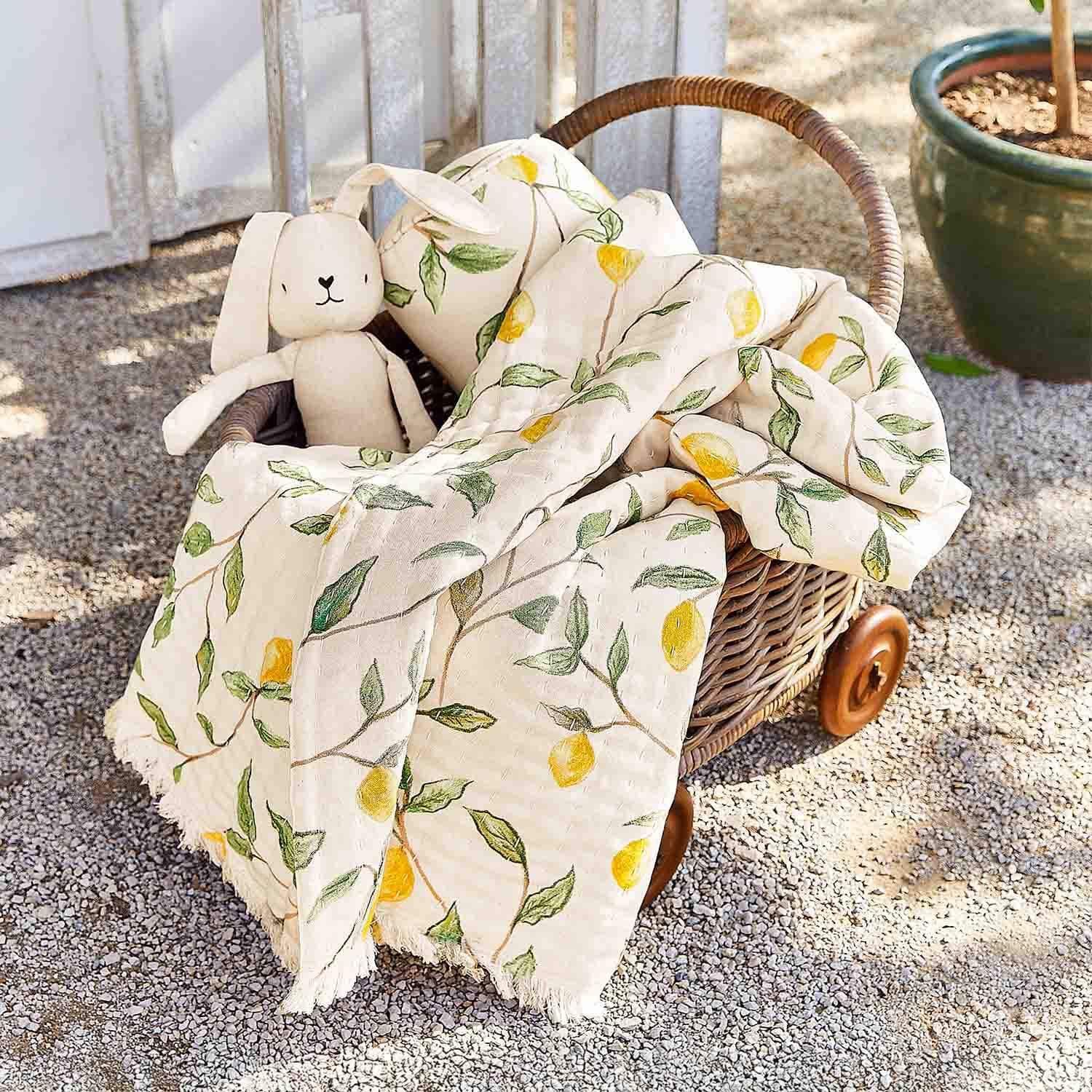 Cesta de mimbre con ruedas con manta de algodón crema con diseño de limones y peluche de conejo