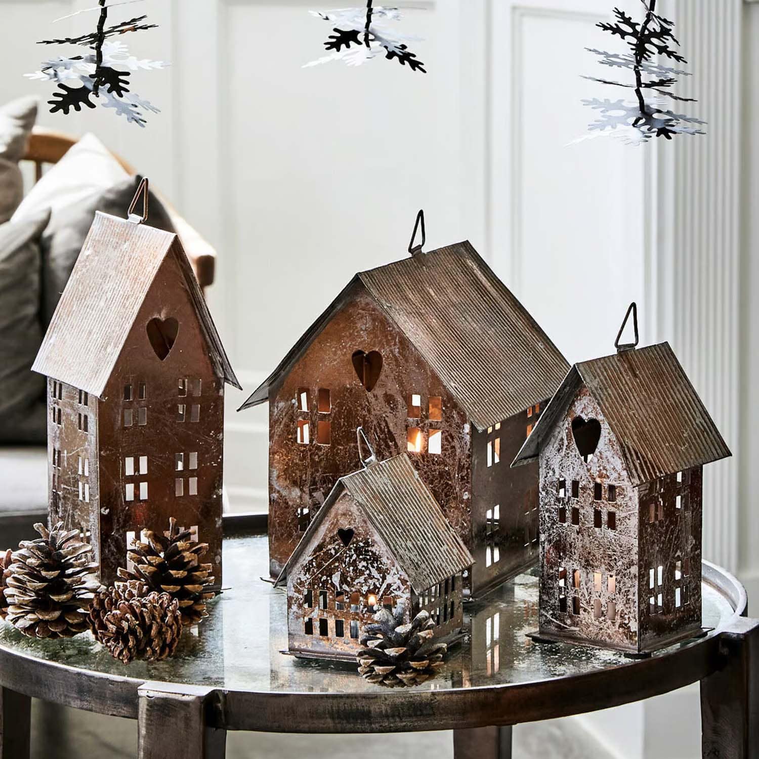 Casitas decorativas de metal con corazones y ventanas recortadas sobre mesa de cristal con piñas