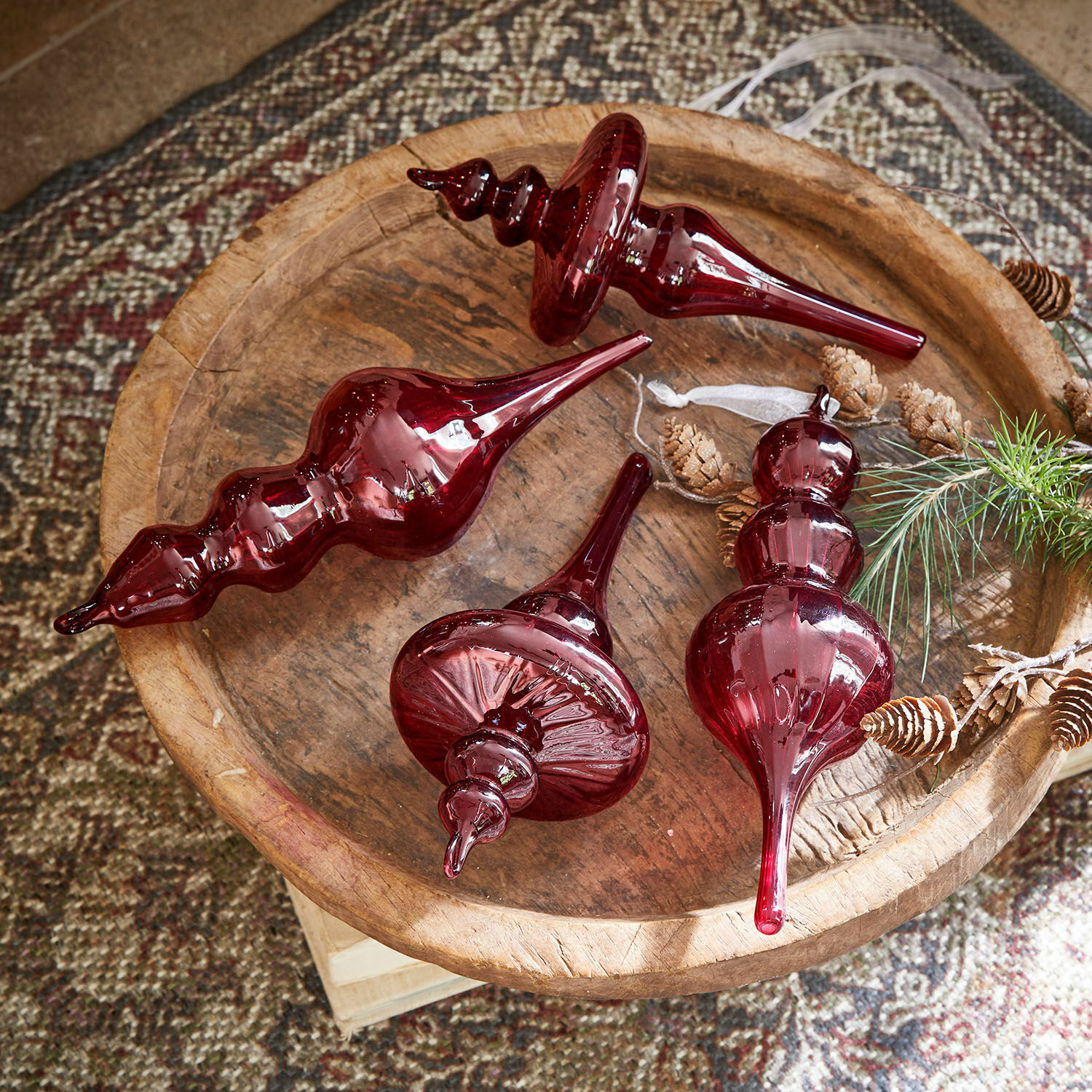 Set de 4 colgantes Camorita Cuatro adornos navideños de vidrio rojo sobre una bandeja de madera con piñas y ramita natural