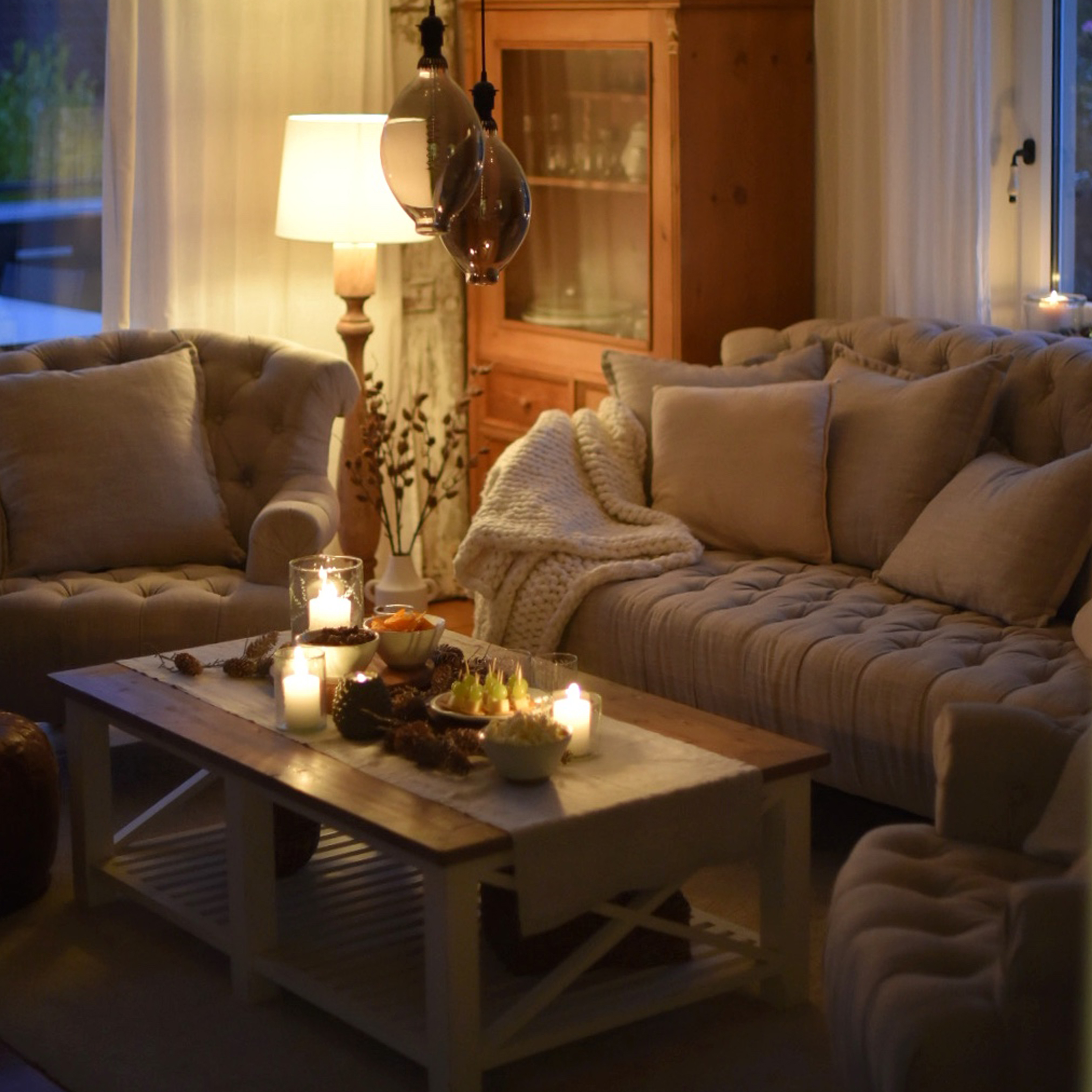 Salón acogedor con sofá beige, sillones y mesa de centro de madera con velas y aperitivos