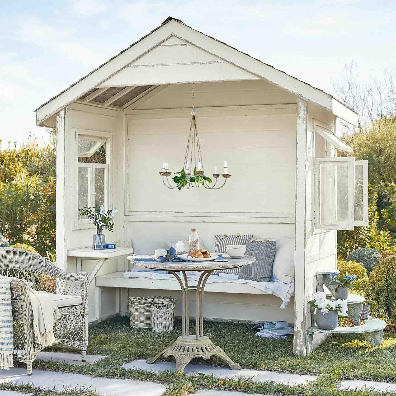 Pérgola de madera blanca con sillón de mimbre y mesa redonda sobre césped