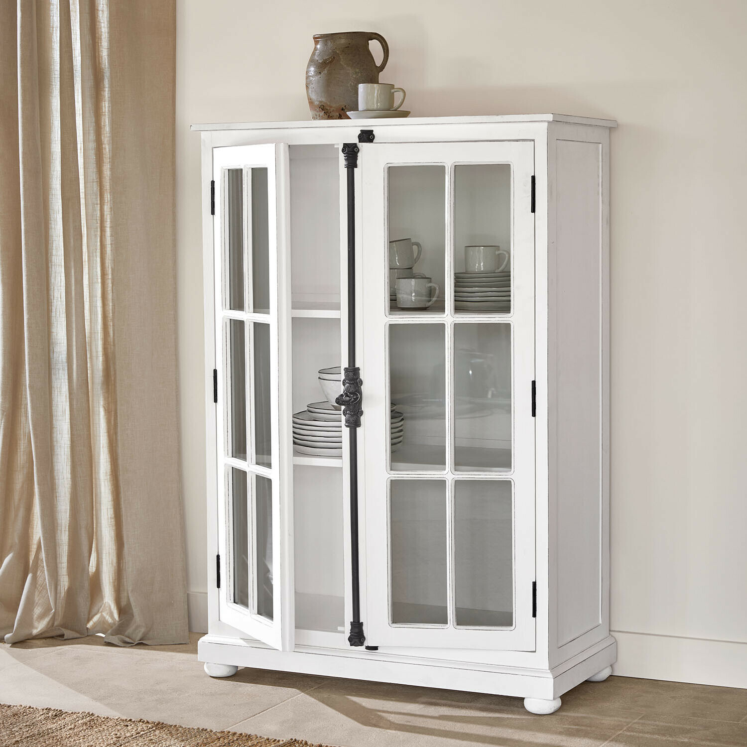 Vitrina Salivonne Vitrina de madera blanca con puertas acristaladas y tiradores metálicos negros estilo vintage en interior luminoso