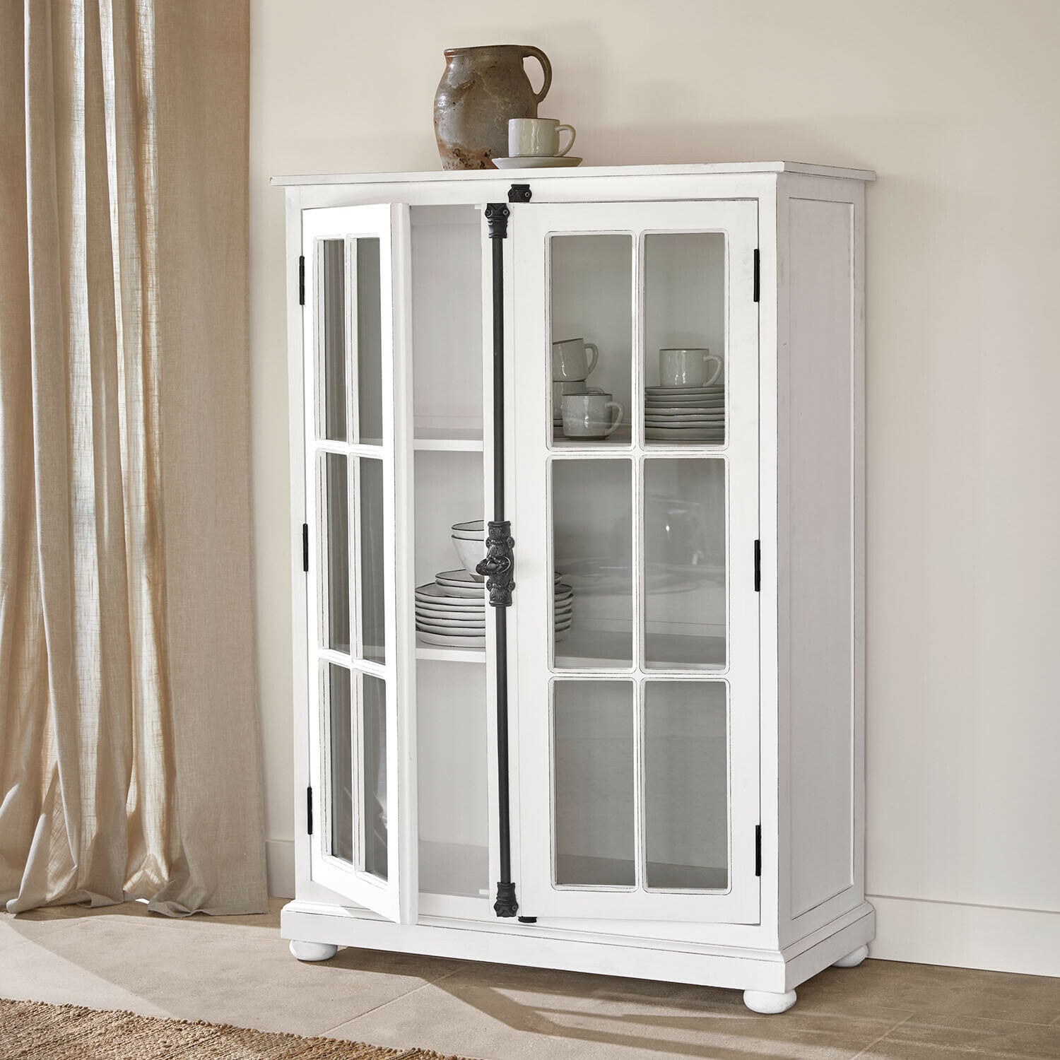 Vitrina Salivonne Vitrina de madera blanca con puertas acristaladas y tiradores metálicos negros estilo vintage en interior luminoso