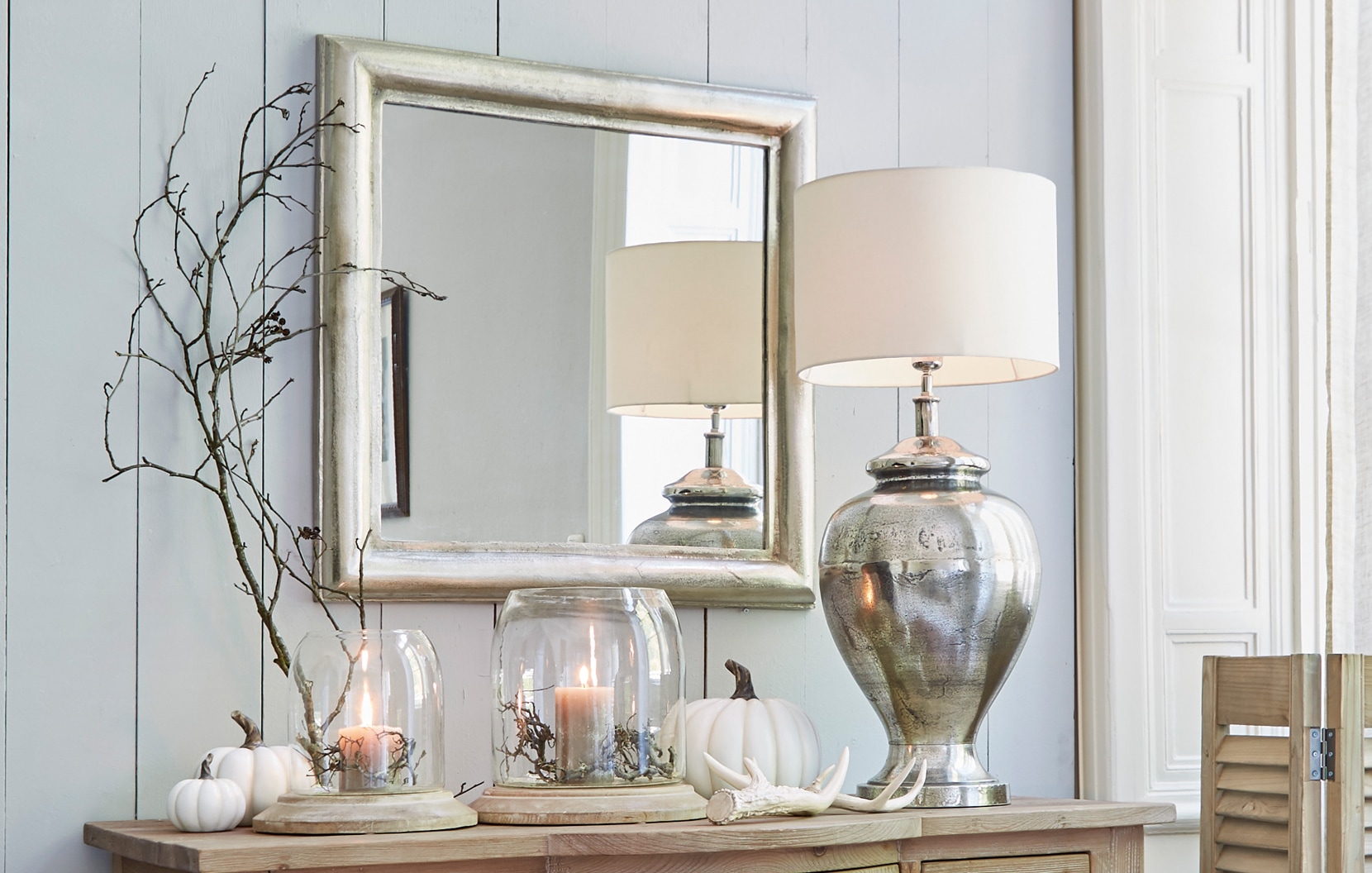 Interior clásico elegante con espejo plateado, lámpara metálica y decoraciones sobre mueble de madera