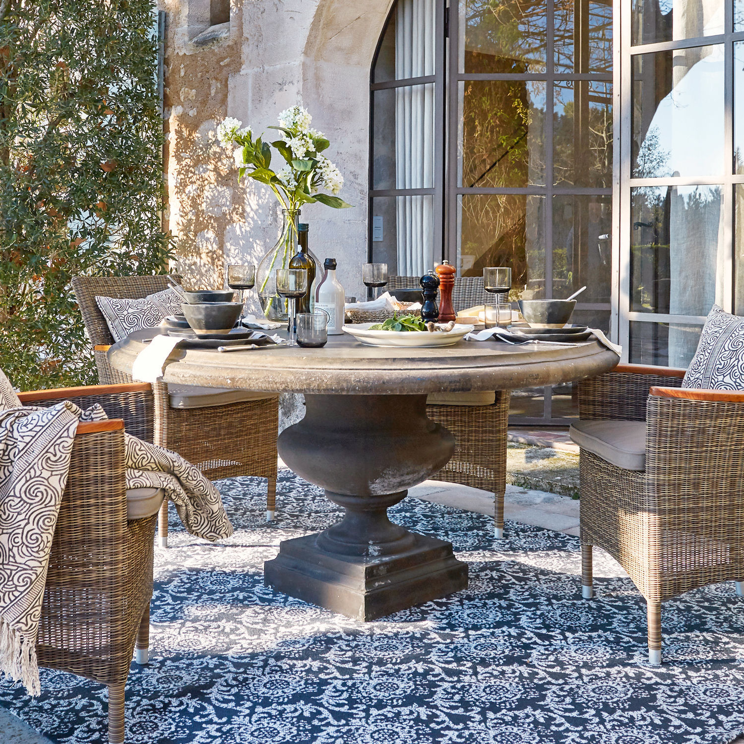 Mesa Monterey Mesa redonda de piedra con base negra y sillas de mimbre en terraza con alfombra decorativa