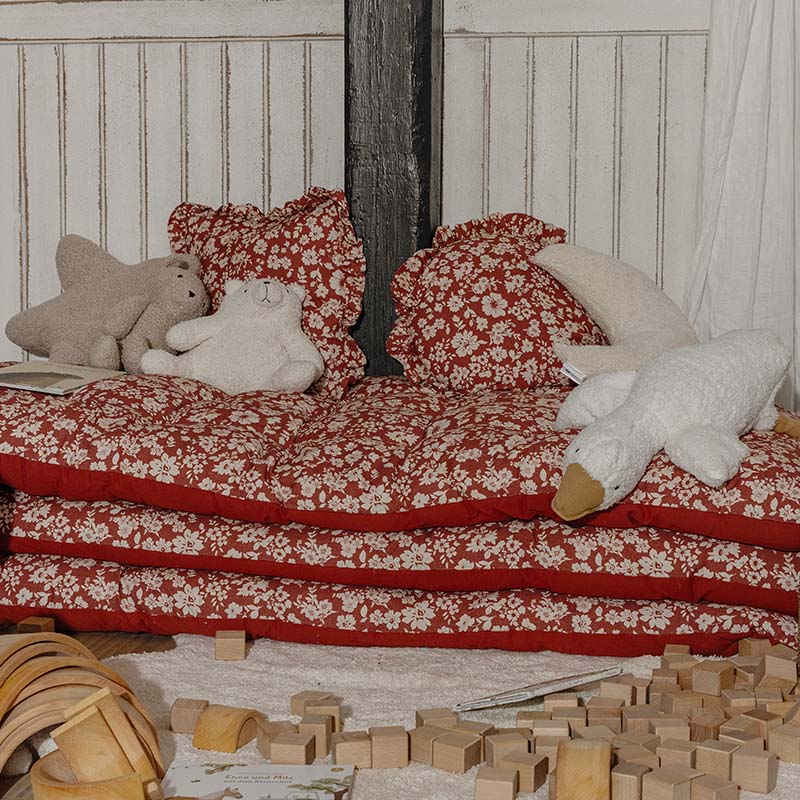 Cojines y colchones rojos con flores y peluches en rincón infantil con bloques de madera para jugar