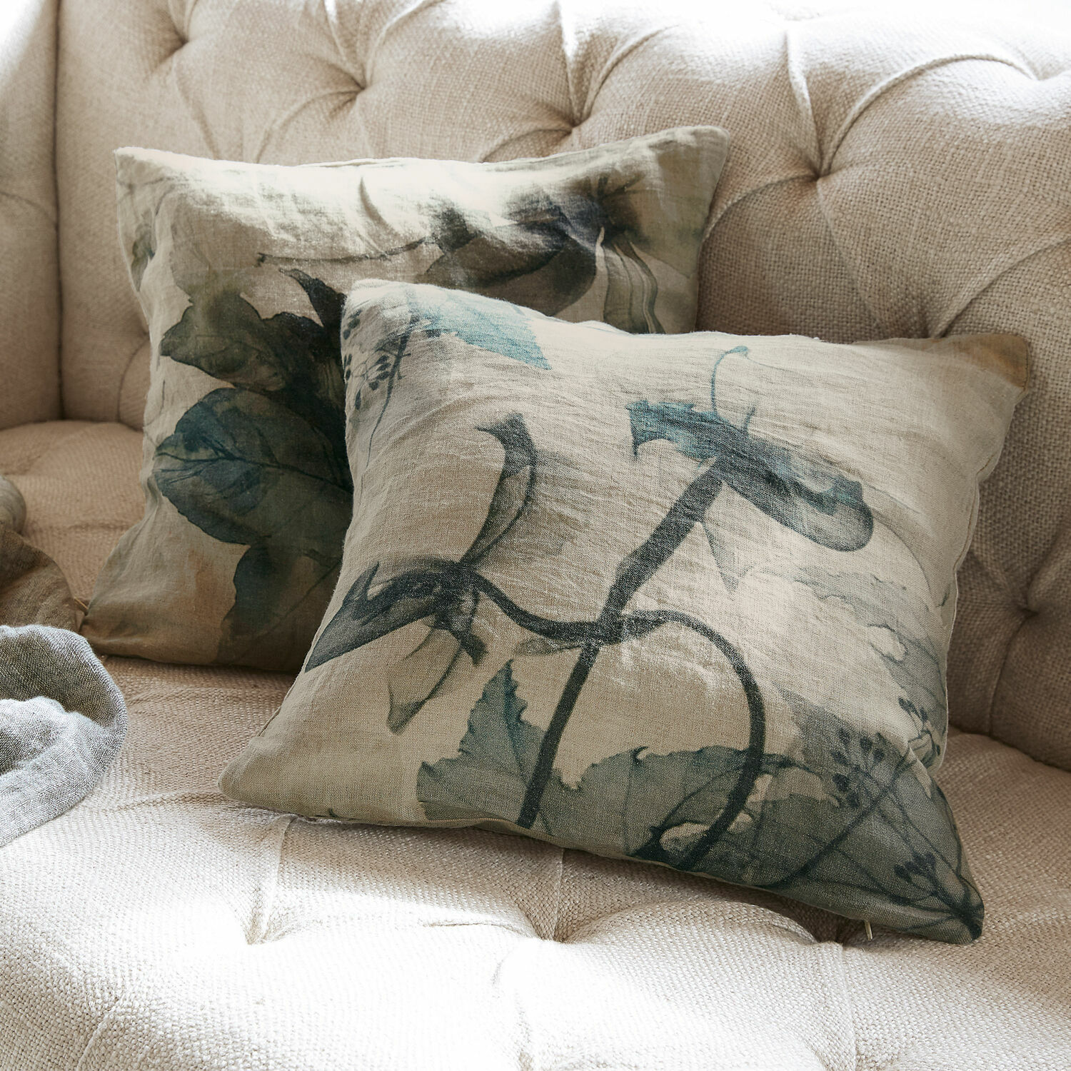 Set de 2 fundas de cojín Forsyth Cojines decorativos de lino beige con hojas verdes sobre sofá claro