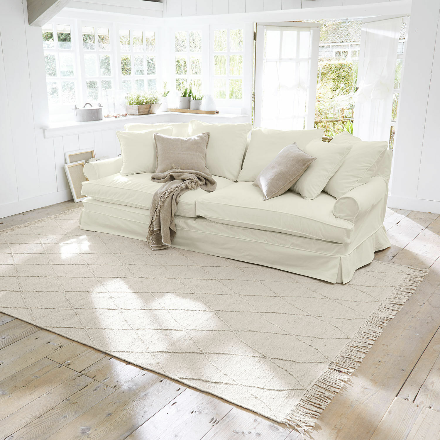 Alfombra Ivonique Sofá beige claro con cojines suaves y manta en sala luminosa de estilo natural