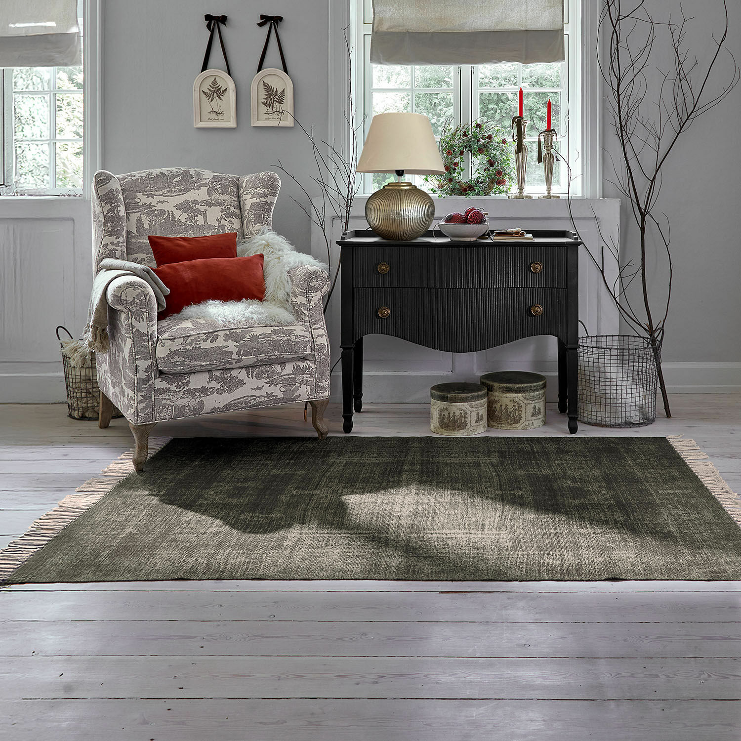 Alfombra para interior y exterior Belaric Sillón acogedor con patrón beige y gris con cojines rojos junto a cómoda negra vintage en sala luminosa