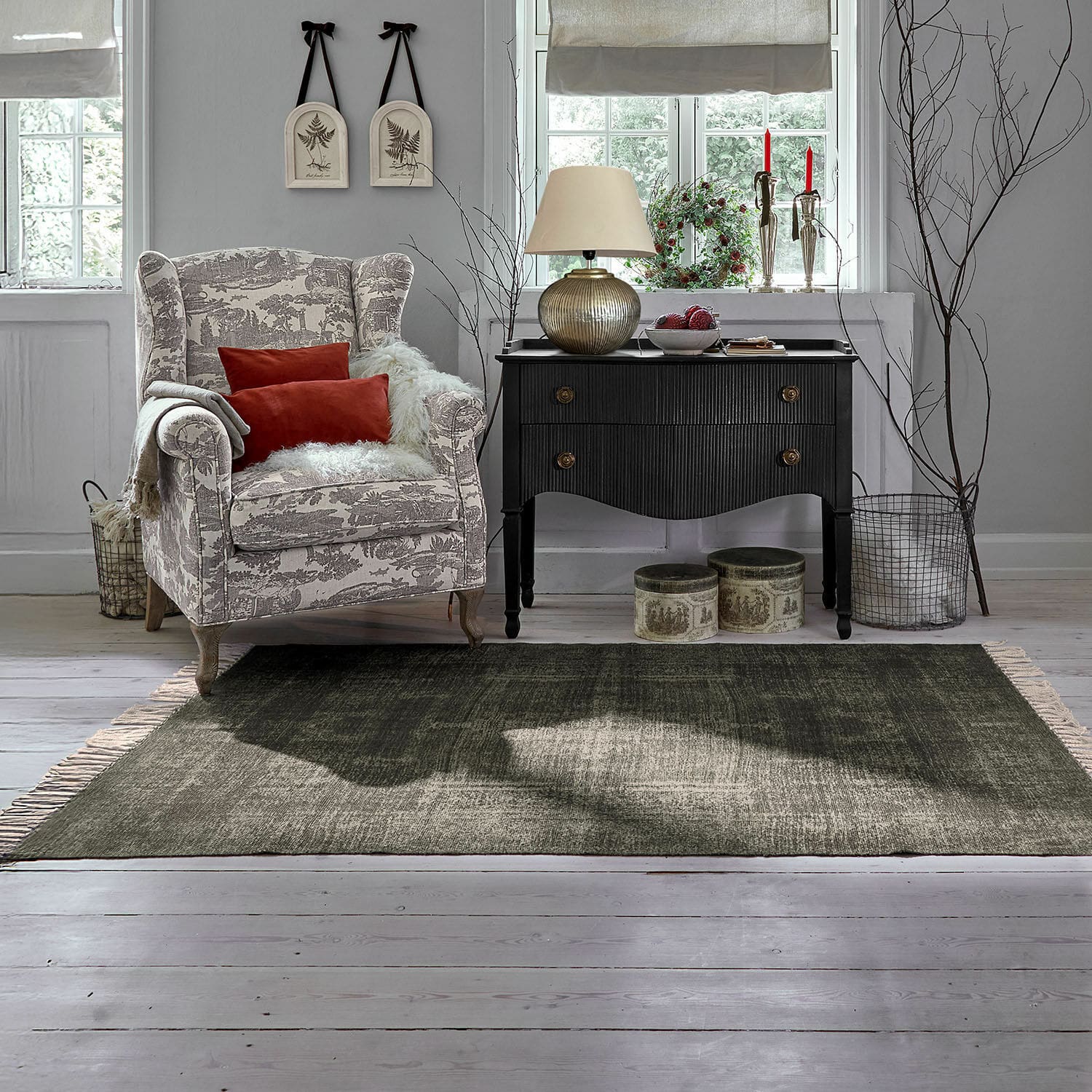 Alfombra para interior y exterior Belaric Sillón acogedor con patrón beige y gris con cojines rojos junto a cómoda negra vintage en sala luminosa