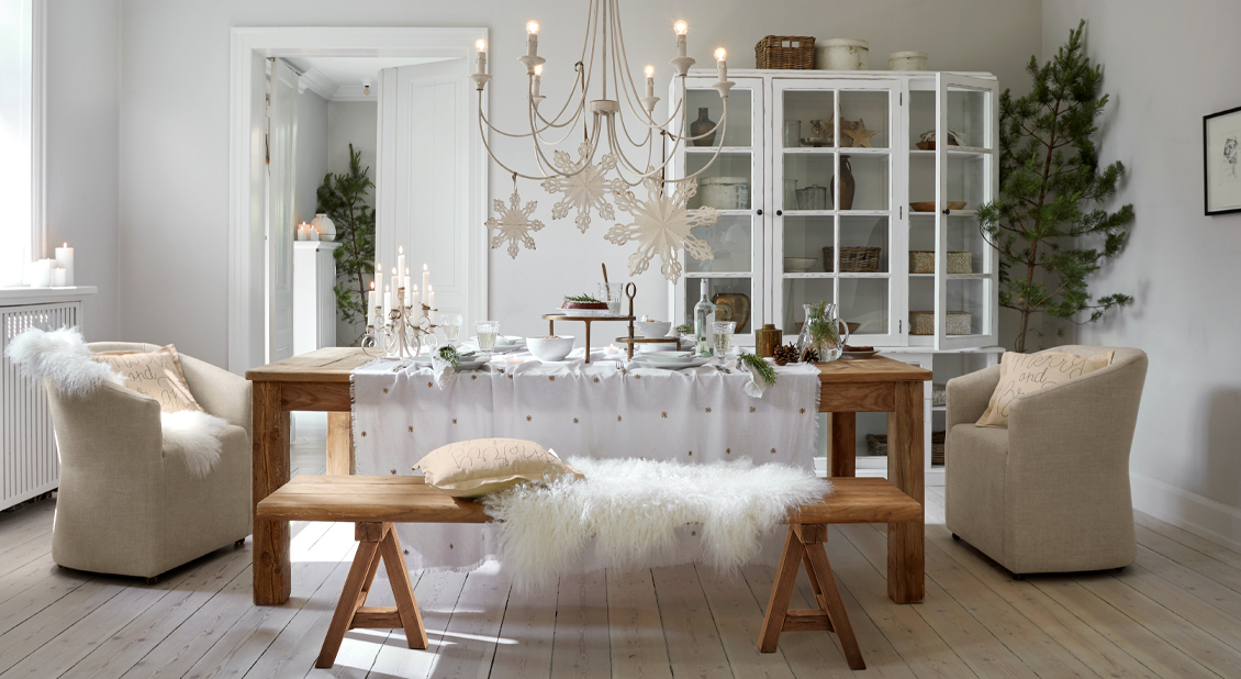 Comedor con mesa de madera, banco, decoración blanca invernal y sillones beige suaves