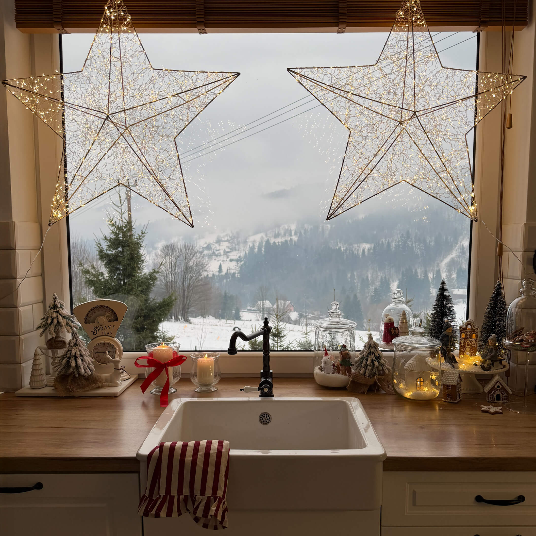 Cocina con fregadero blanco, encimera de madera, decoraciones navideñas y vista de paisaje invernal