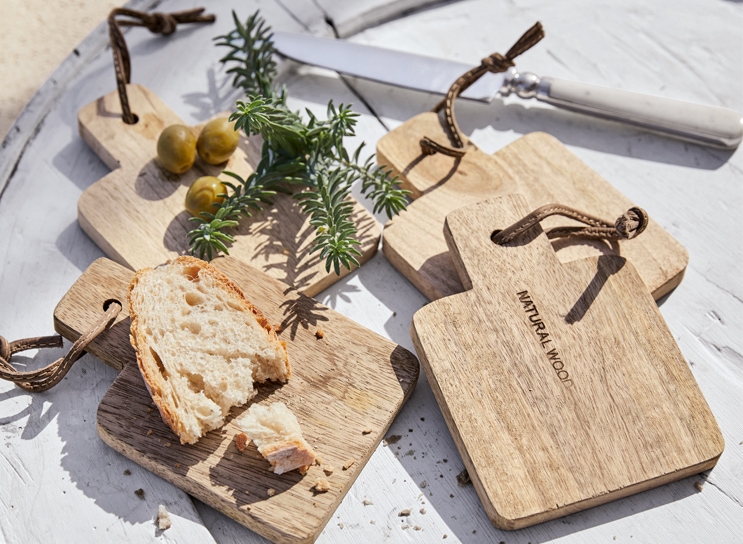 Juego de tablas de cortar de madera natural con pan y aceitunas sobre mesa blanca estilo mediterráneo