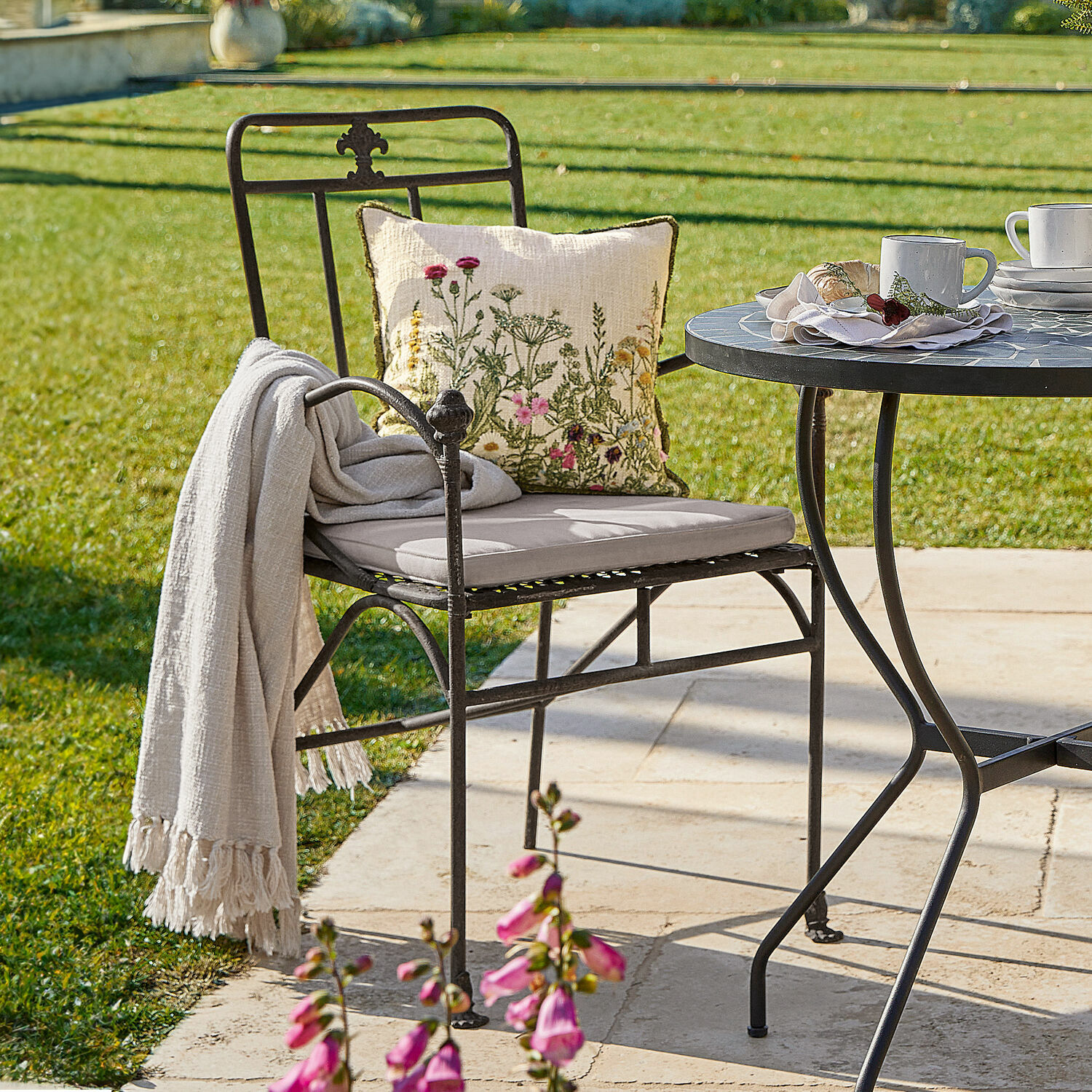 Silla de jardín de metal negro con cojín claro y cojín decorativo floral en terraza soleada