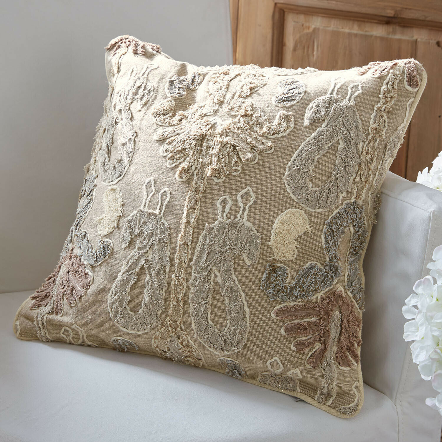 Cojín decorativo beige con diseño bordado en colores naturales sobre sofá blanco
