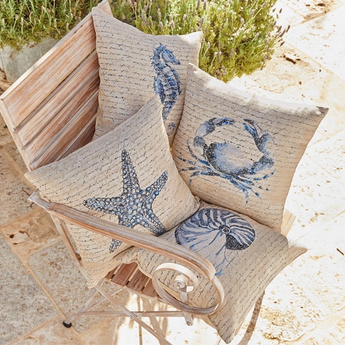 Cuatro cojines beige con motivos marinos y texto, sobre una silla de madera de exterior