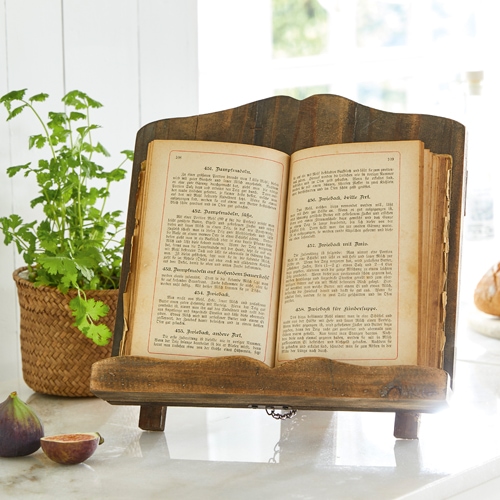 Soporte de libro de cocina de madera en color natural sobre encimera clara con planta e higos