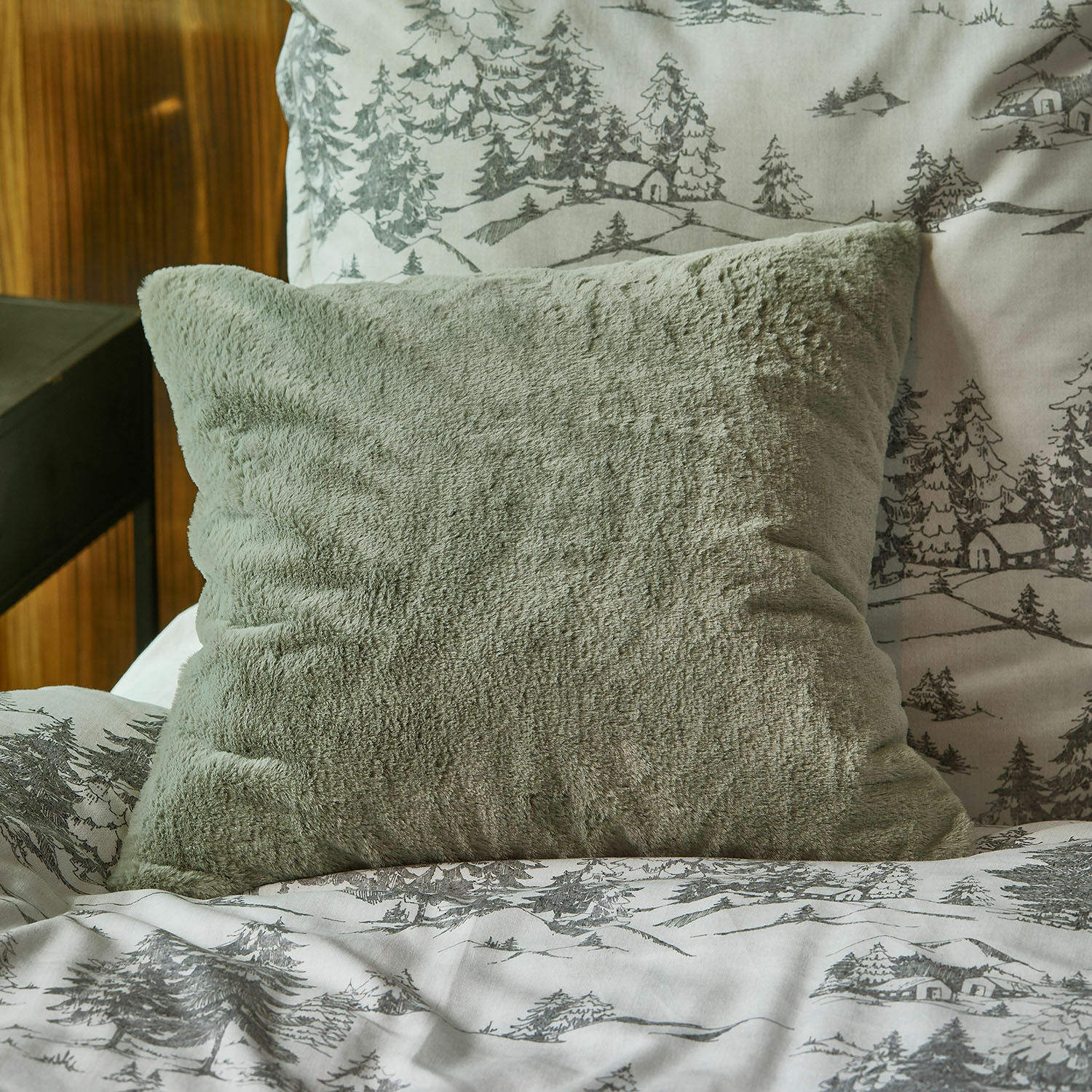 Funda de cojín Léorienne Cojín verde de felpa suave sobre cama con funda de edredón con estampado gris de árboles y casas