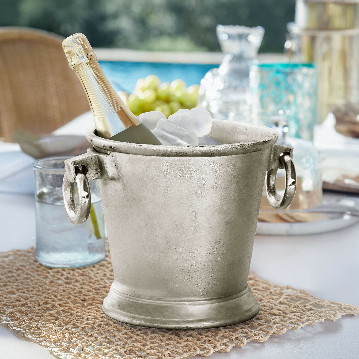 Enfriador de bebidas Cressford Cubitera metálica plateada con botella de champán y hielo sobre mesa de jardín