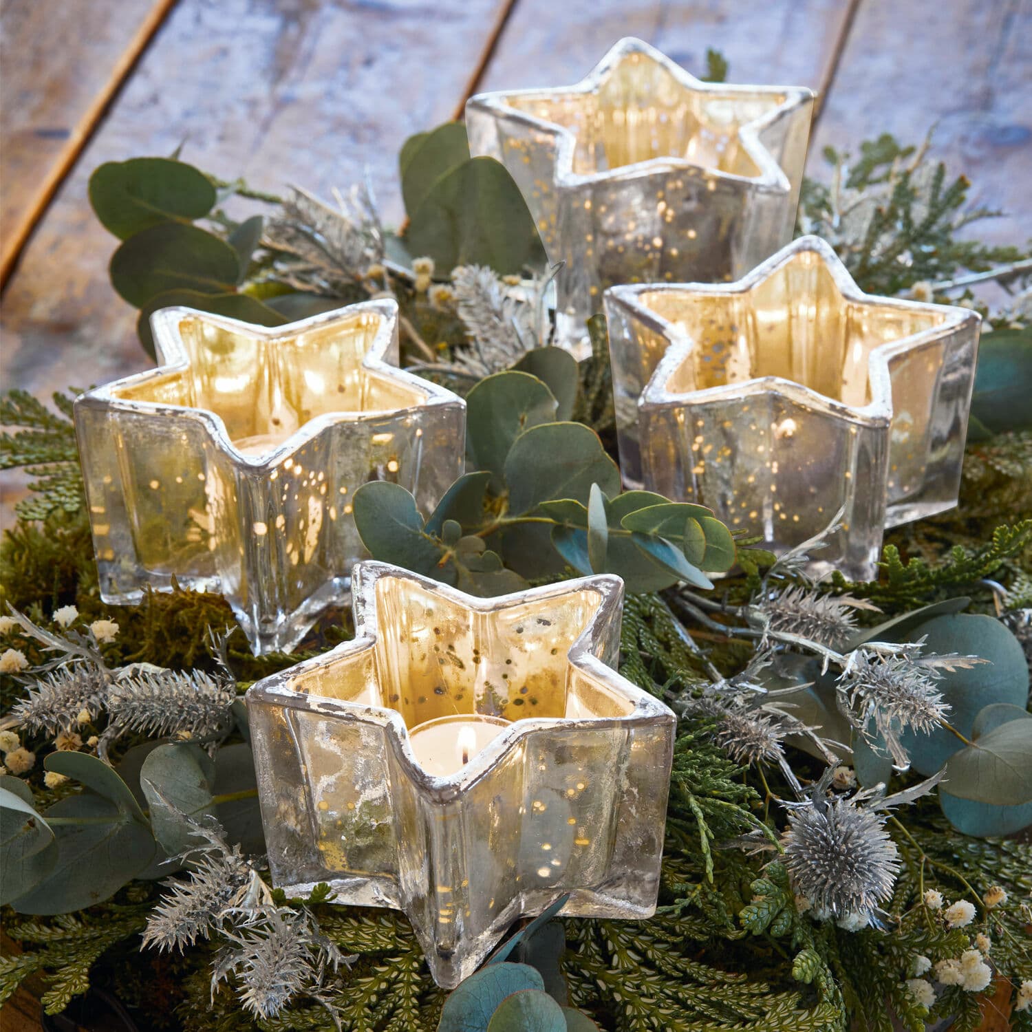 Set de 4 farolillos para clavar Bernice Portavelas de vidrio en forma de estrella con efecto espejo plateado sobre fondo decorativo verde
