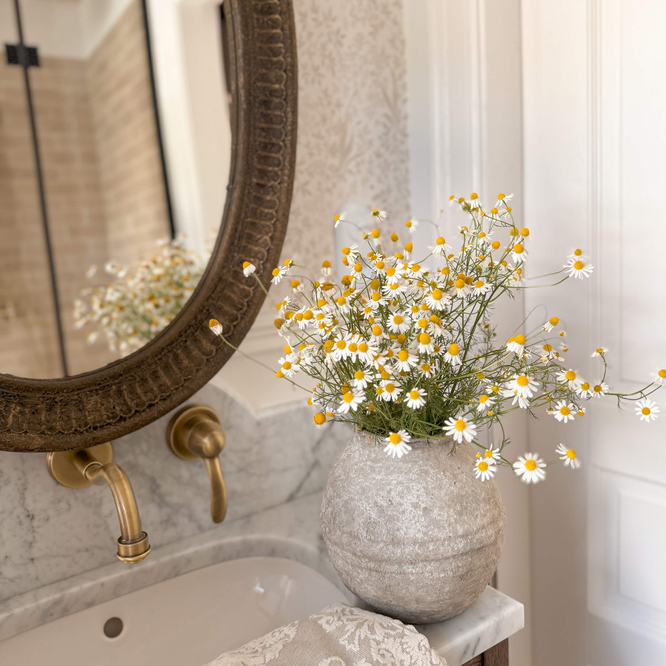 Jarrón de piedra gris con flores blancas y amarillas sobre lavabo de mármol en baño elegante