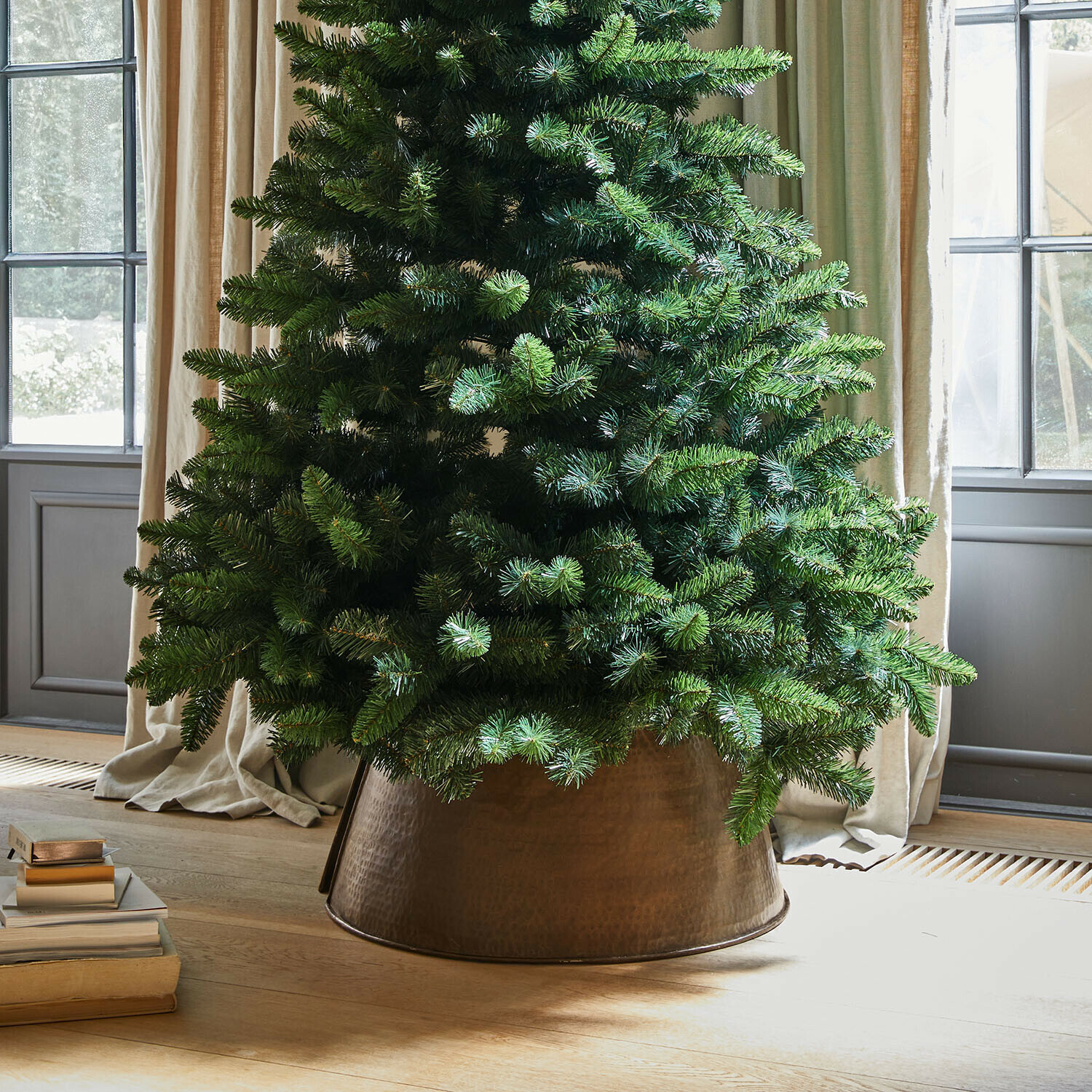 Base para árbol de Navidad Omeyra Árbol de Navidad artificial en maceta metálica de cobre sobre suelo de madera clara junto a libros
