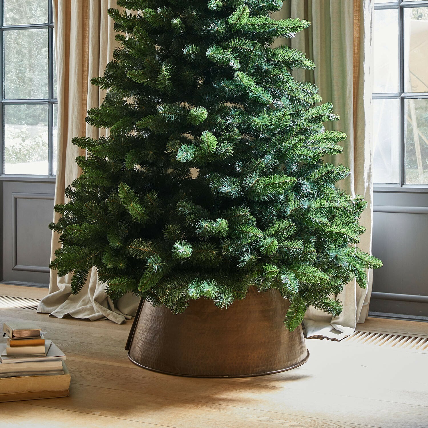 Base para árbol de Navidad Omeyra Árbol de Navidad artificial en maceta metálica de cobre sobre suelo de madera clara junto a libros