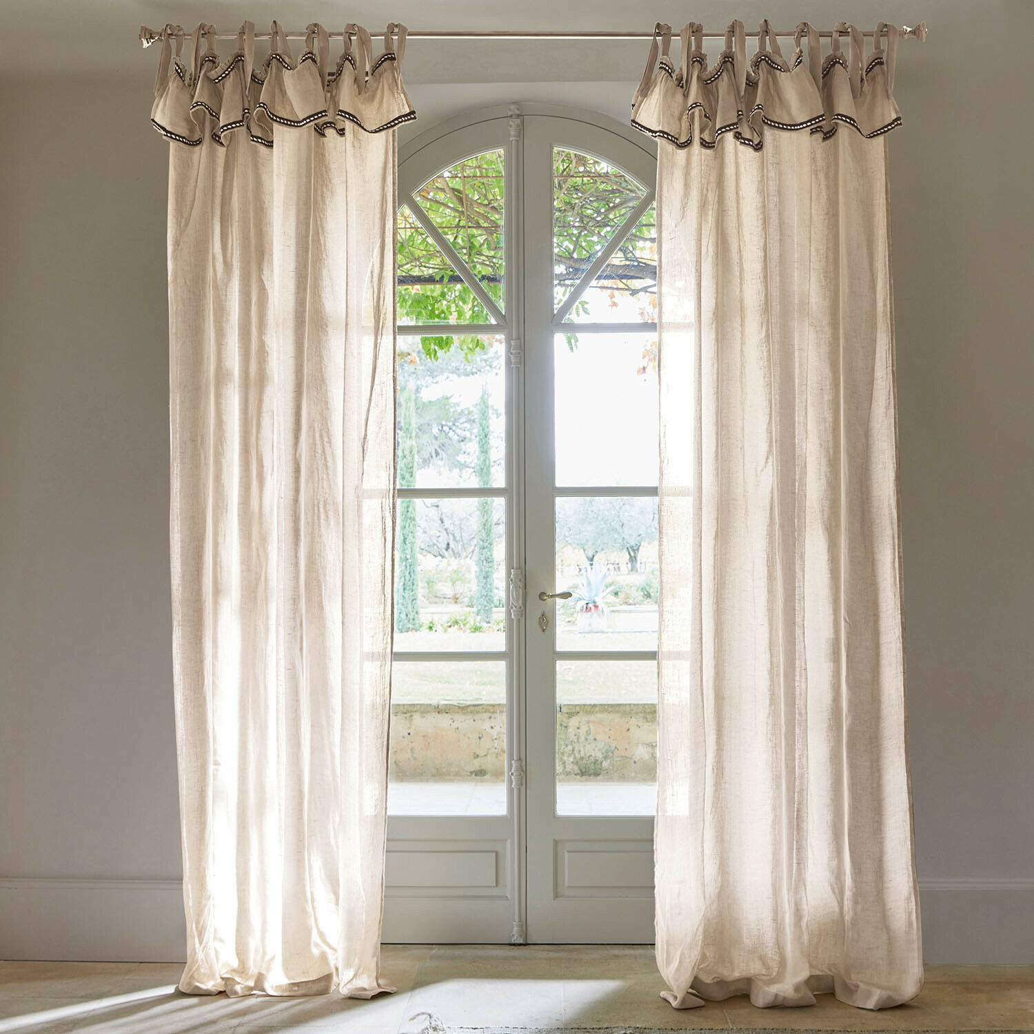 Cortina Romagny Cortinas de lino beige con borde decorativo colgadas en ventana con vista al jardín, decoración interior