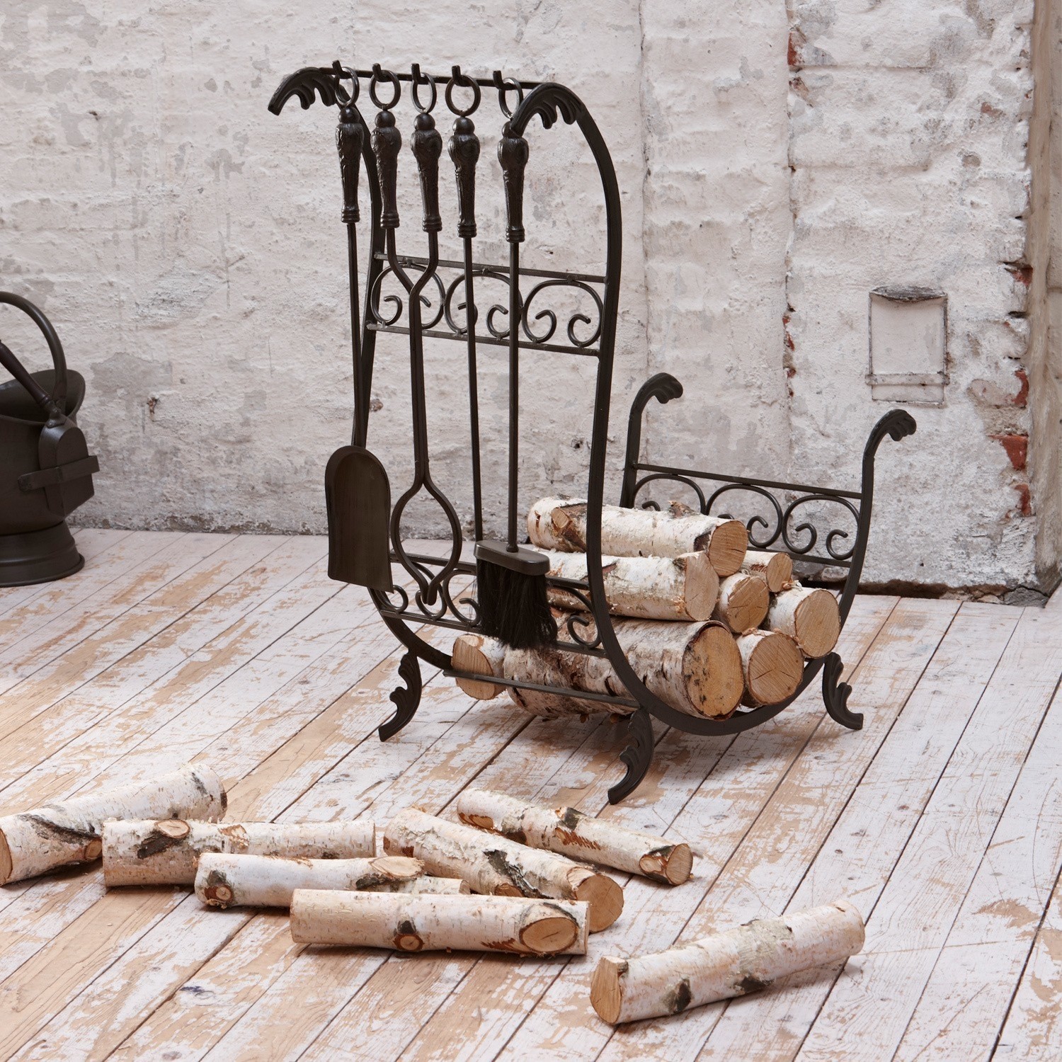 Estante de leña Stirling Soporte metálico para leña con herramientas de chimenea y troncos de abedul blanco sobre suelo de madera