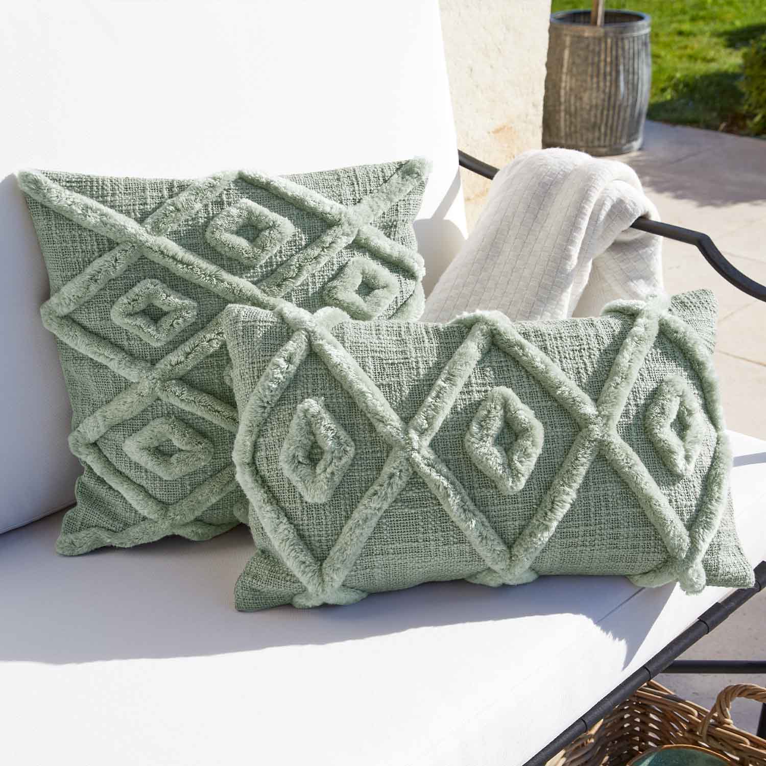 Cojín decorativo verde suave con diseño geométrico sobre silla blanca de jardín