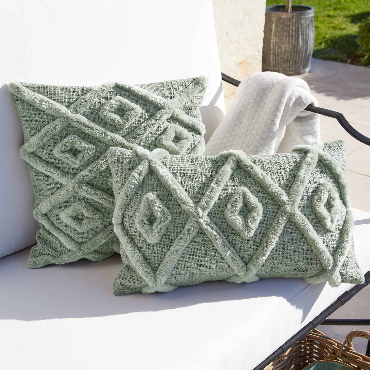 Cojín decorativo verde suave con diseño geométrico sobre silla blanca de jardín