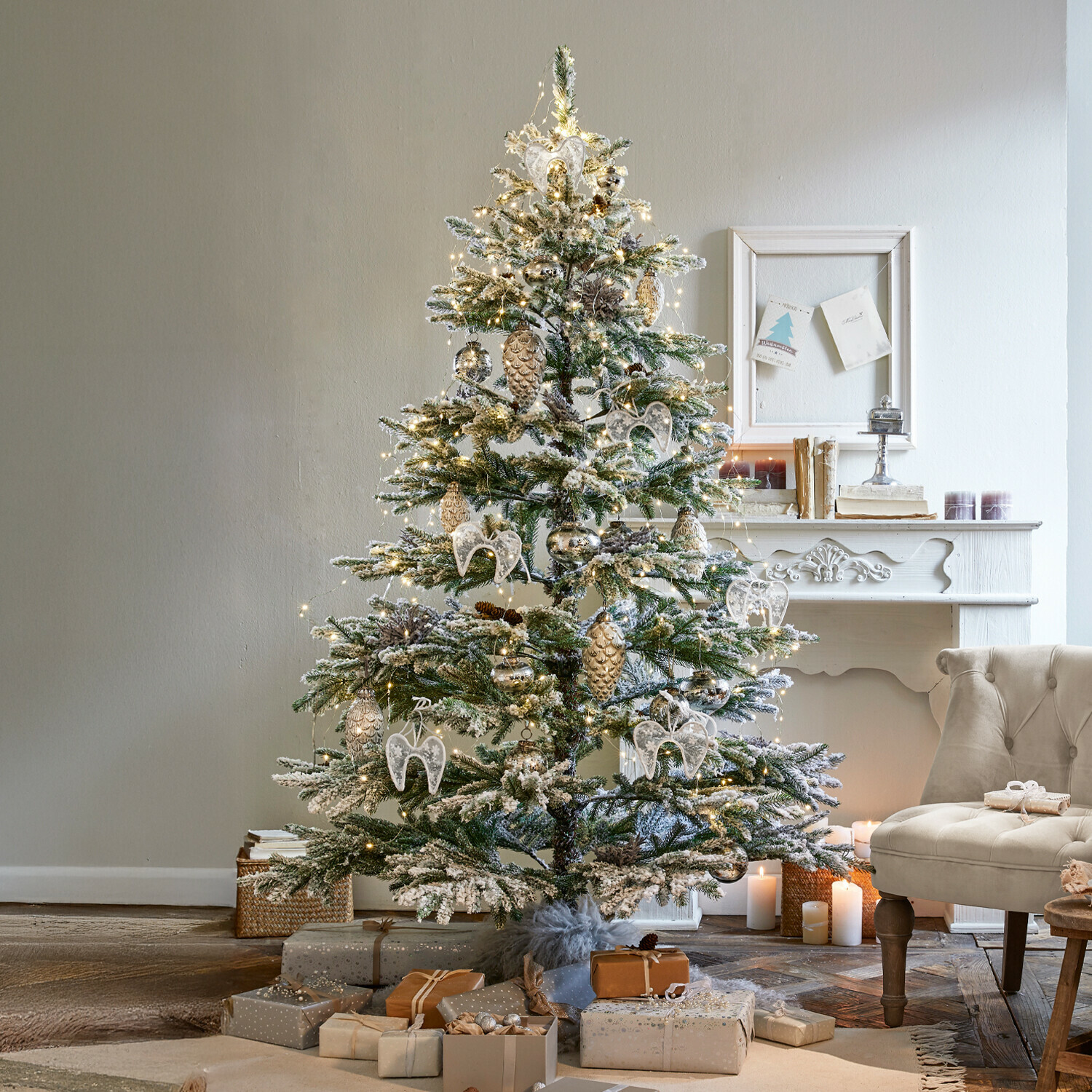 Árbol de Navidad Lokossa Árbol de Navidad nevado con adornos blancos y dorados y regalos junto a un sillón beige en una sala acogedora