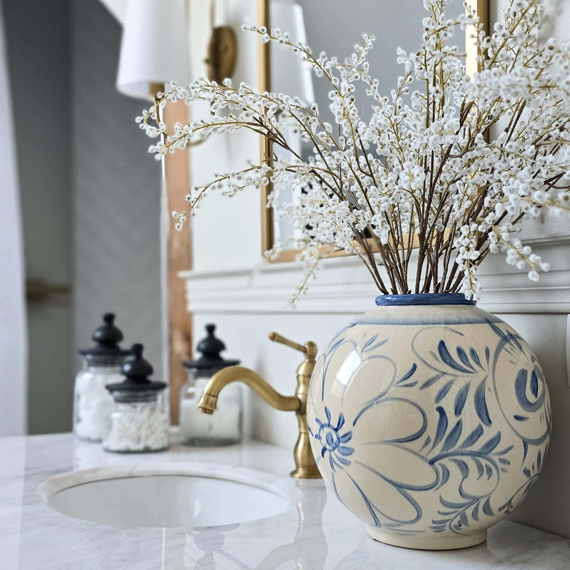 Jarrón redondo de cerámica con diseño floral azul sobre encimera de mármol en baño decorado