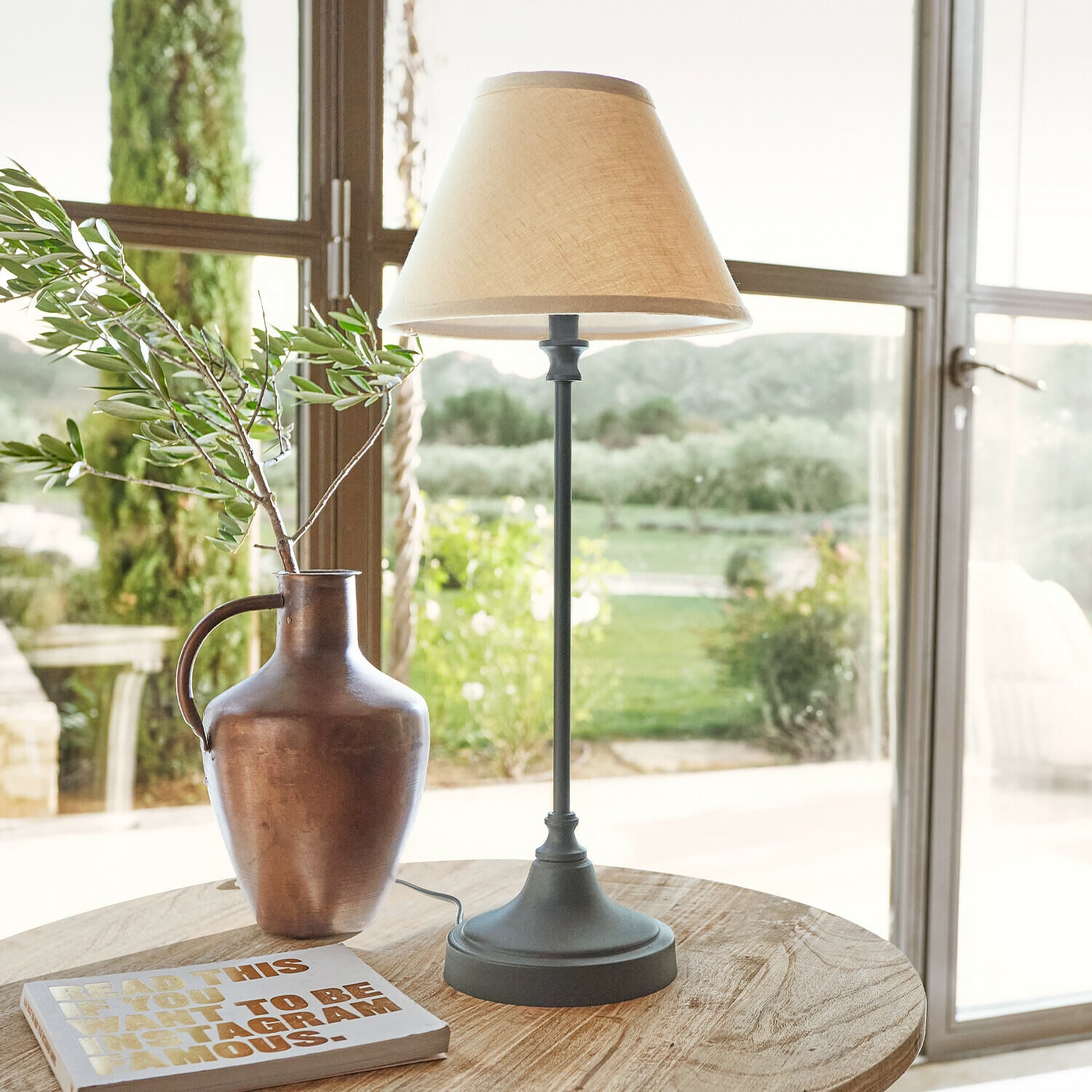 Lámpara de mesa Swindon Lámpara de mesa con base metálica y pantalla beige sobre mesa de madera con jarrón y libro
