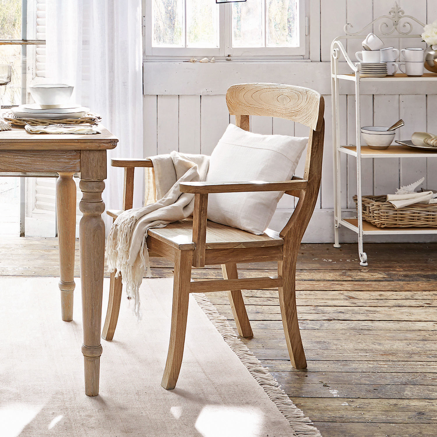 Silla con reposabrazos Masters Silla de madera clara con reposabrazos, cojín blanco y manta en un interior acogedor y luminoso