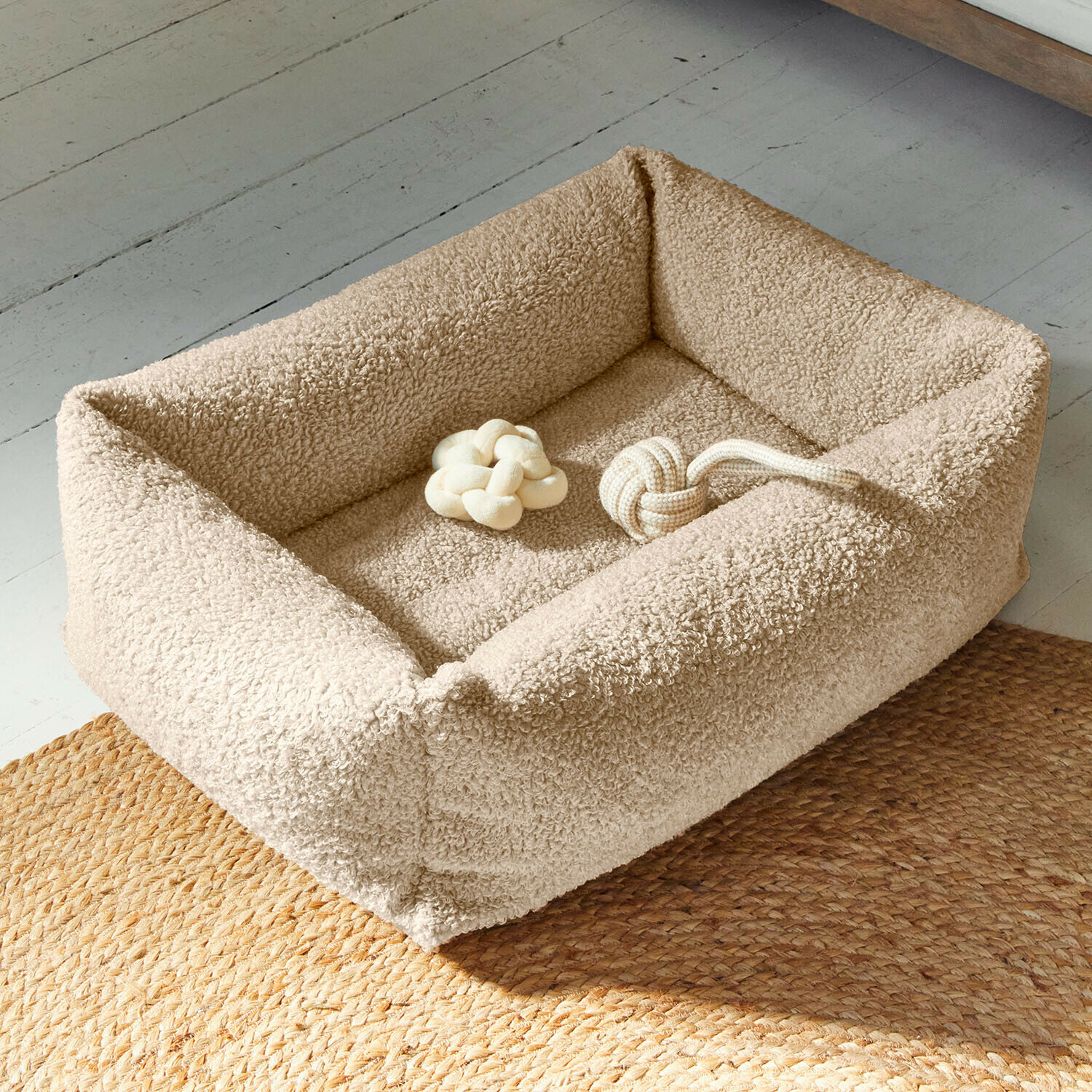 Cama para mascotas Giolena Cama para perro beige de material suave con dos juguetes de nudos beige sobre suelo con alfombra trenzada