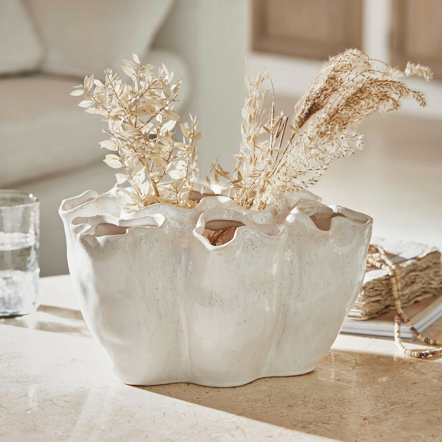 Jarrón Rovinia Jarrón de cerámica blanca con borde ondulado y plantas secas sobre mesa decorativa