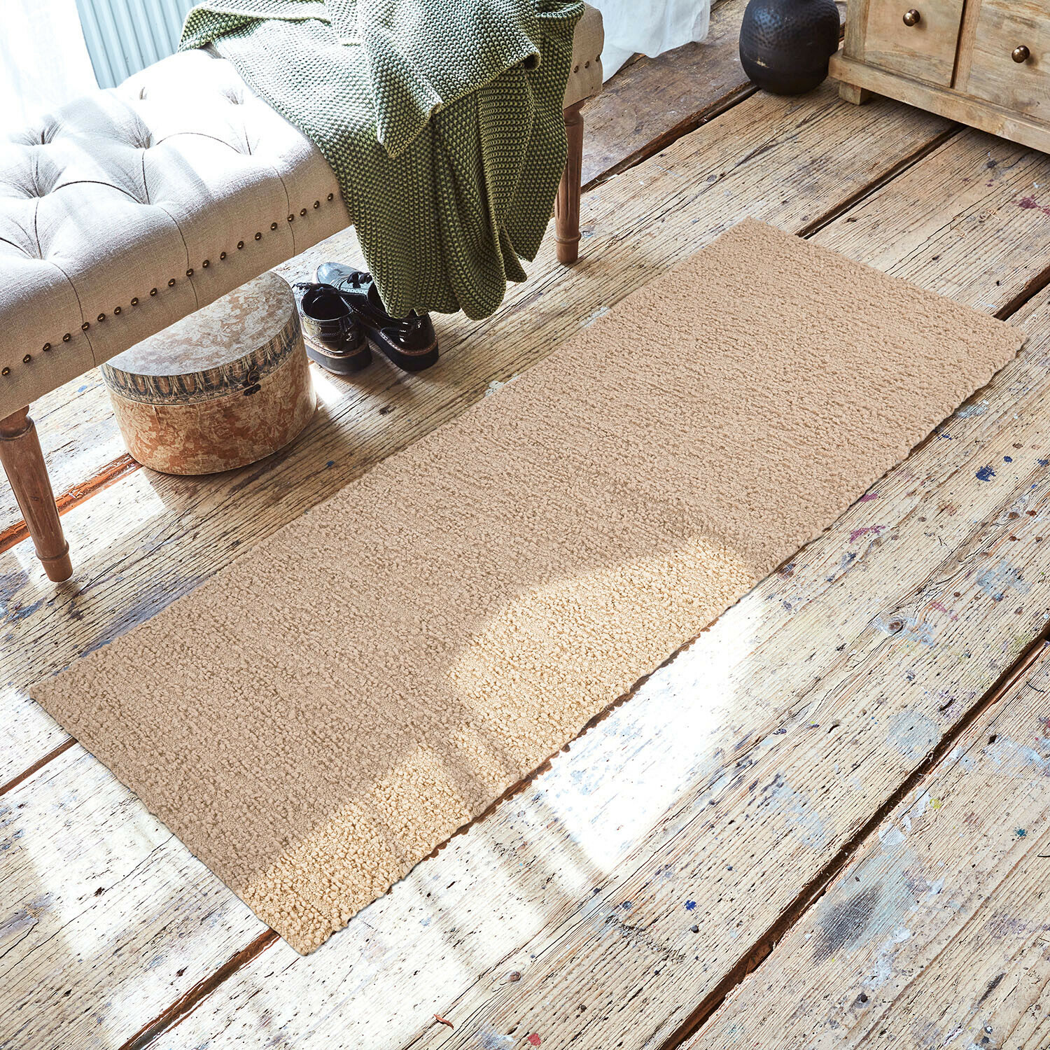 Alfombra Kaleema Alfombra beige de material suave sobre suelo de madera en interior acogedor con banco y manta verde