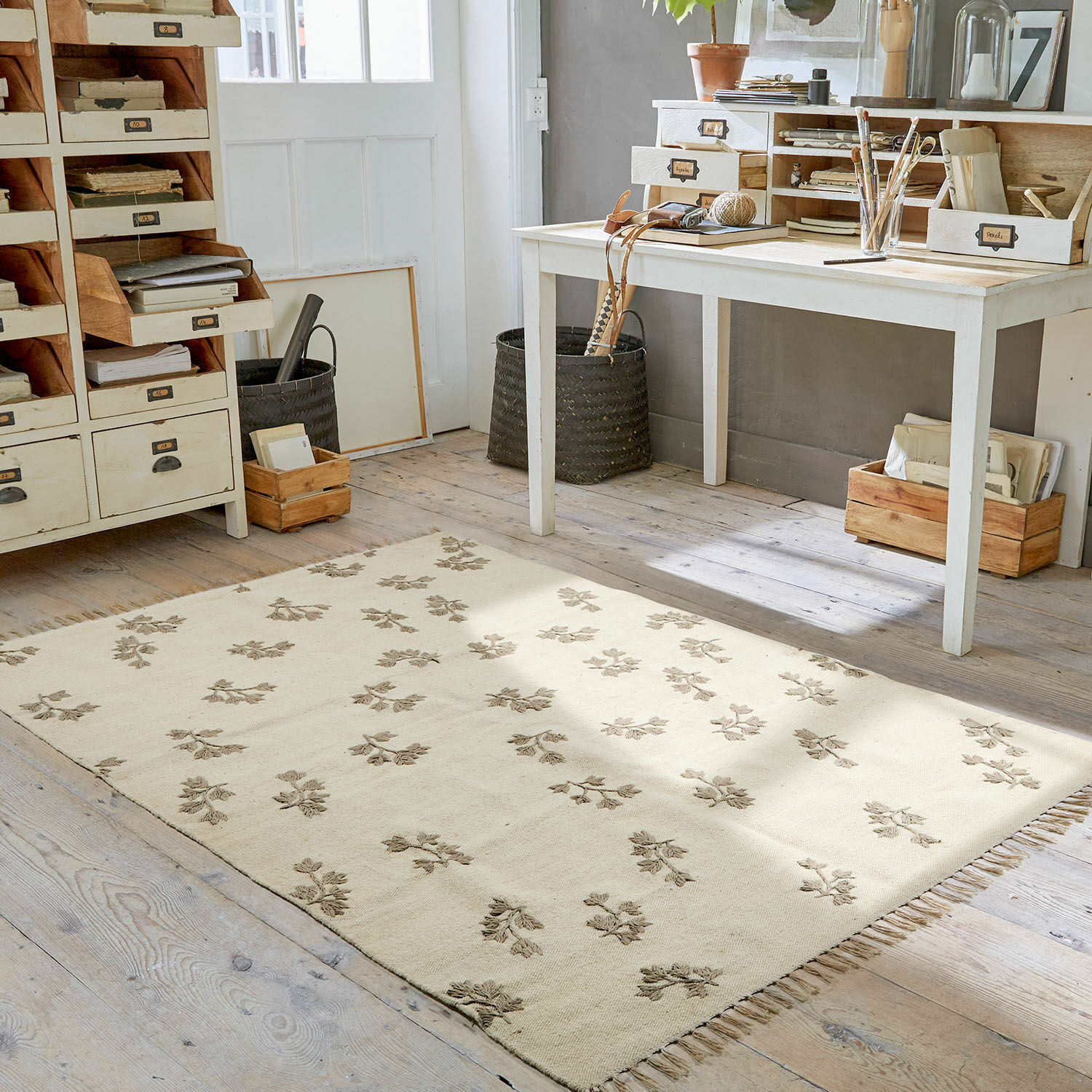 Alfombra beige con diseño floral y flecos sobre suelo de madera en habitación luminosa de trabajo