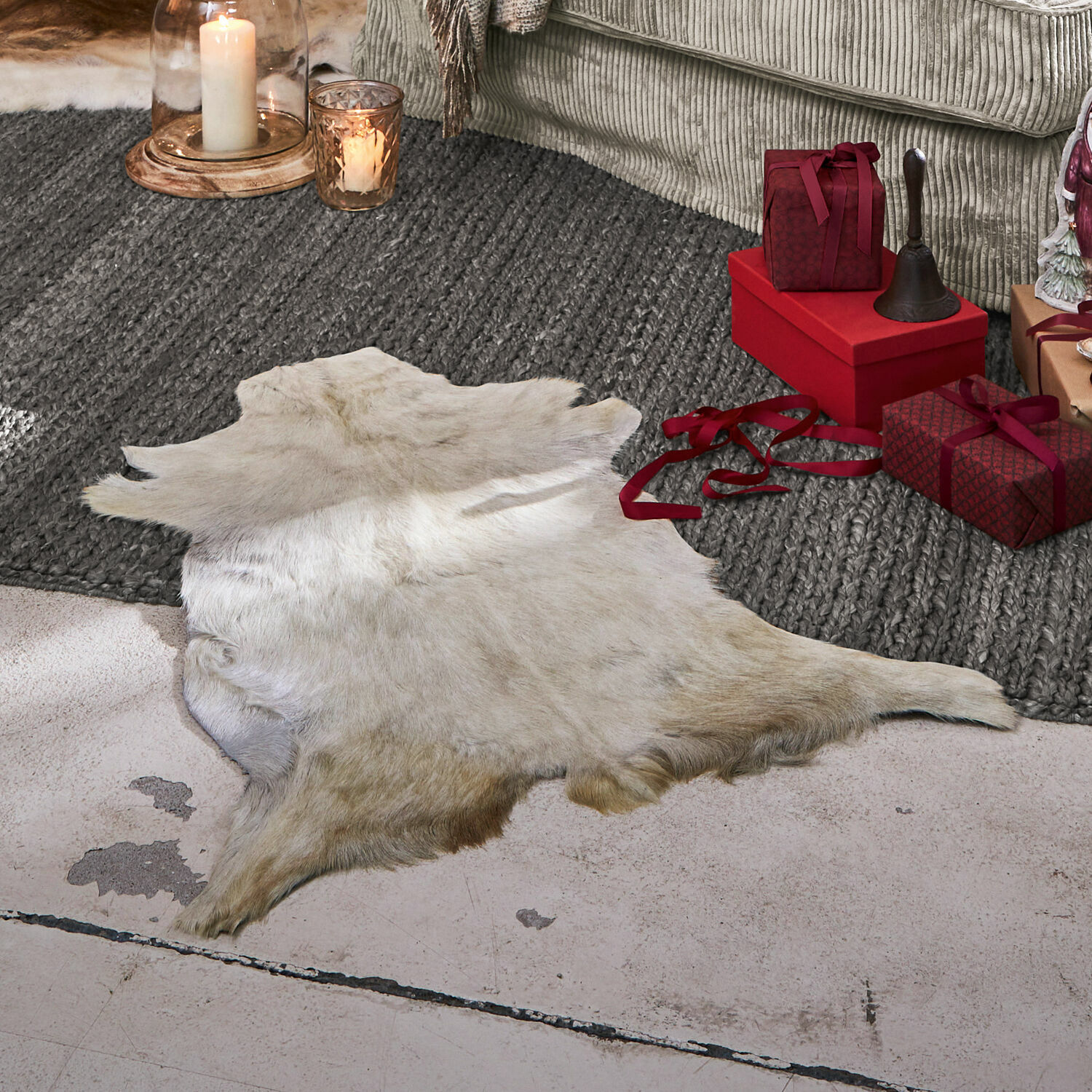 Alfombra de piel de cabra Piedro Piel natural blanca sobre el suelo junto a regalos rojos y velas en una sala de estar