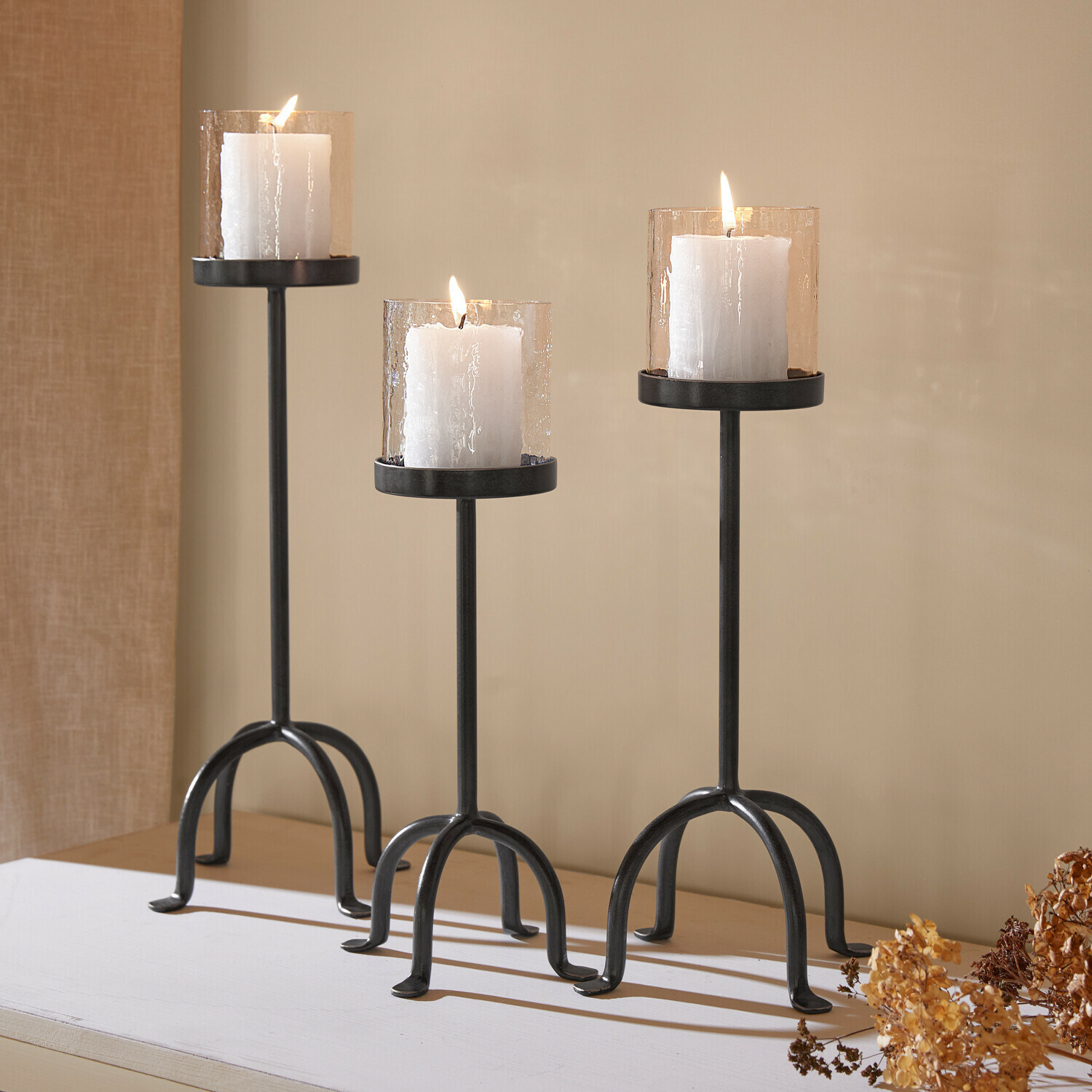 Set de 3 candeleros Tanbira Conjunto de tres candelabros de metal negro con velas blancas y pantallas de vidrio texturizado