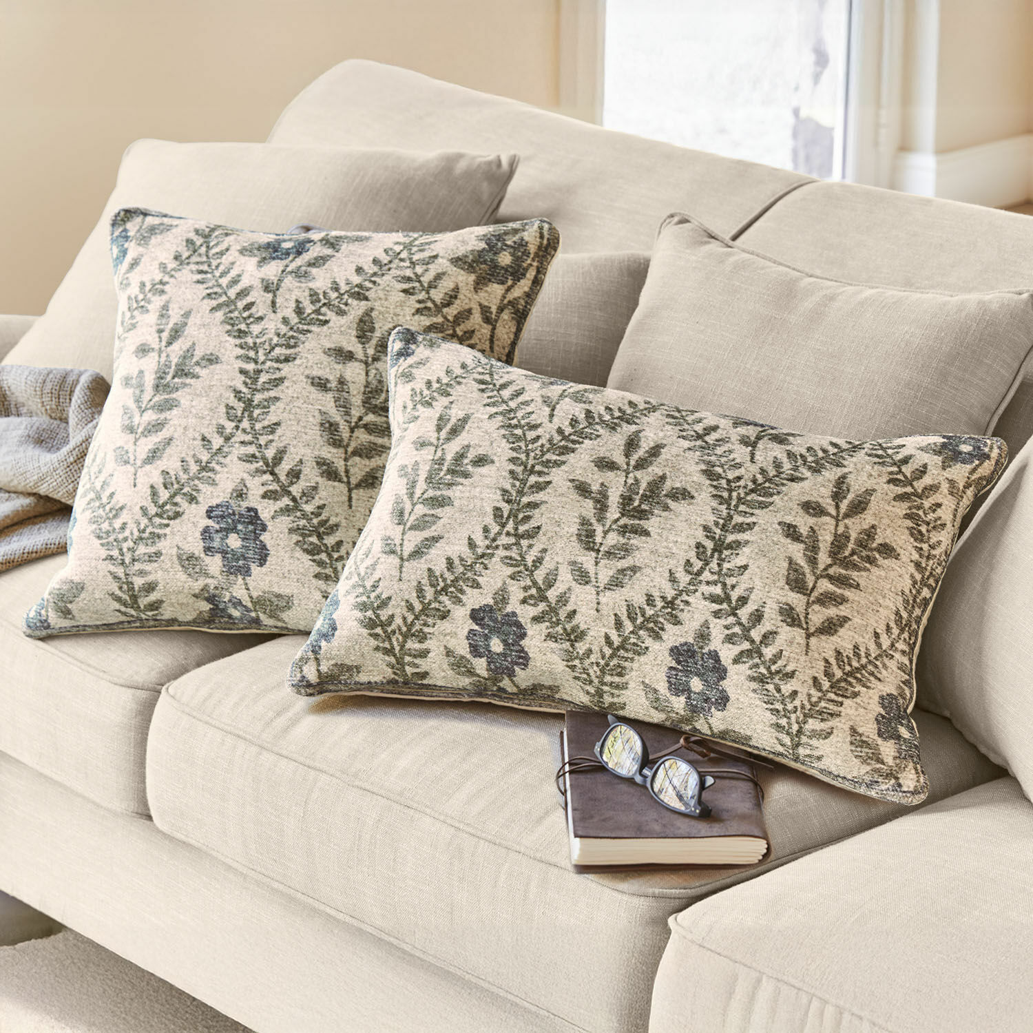 Set de 2 fundas de cojín Vellouris Sofá beige con dos cojines decorativos con patrón de hojas verdes y flores, tela suave