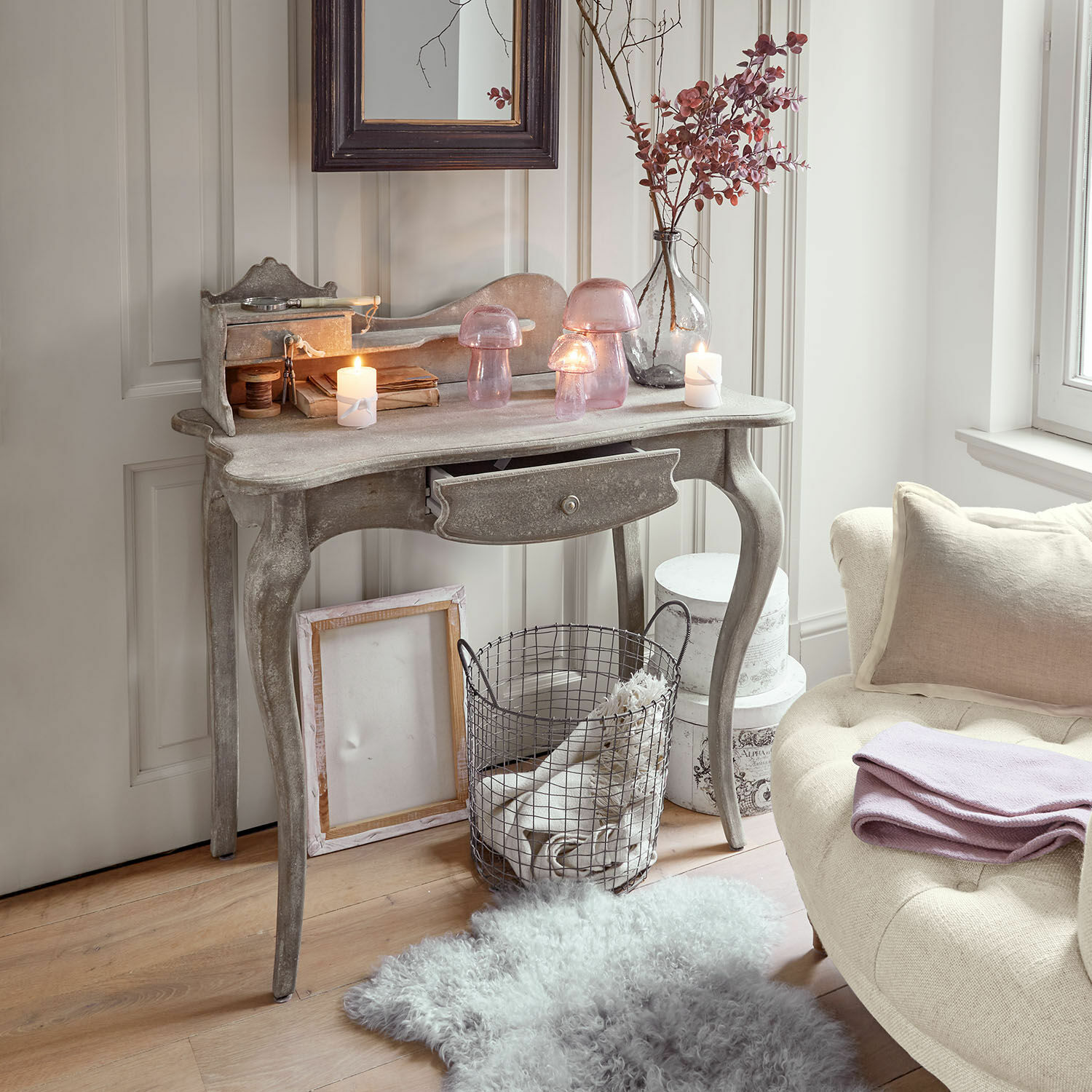 Consola Loustain Consola de madera gris con cajón, decorada con faroles de vidrio rosa y velas en un interior acogedor