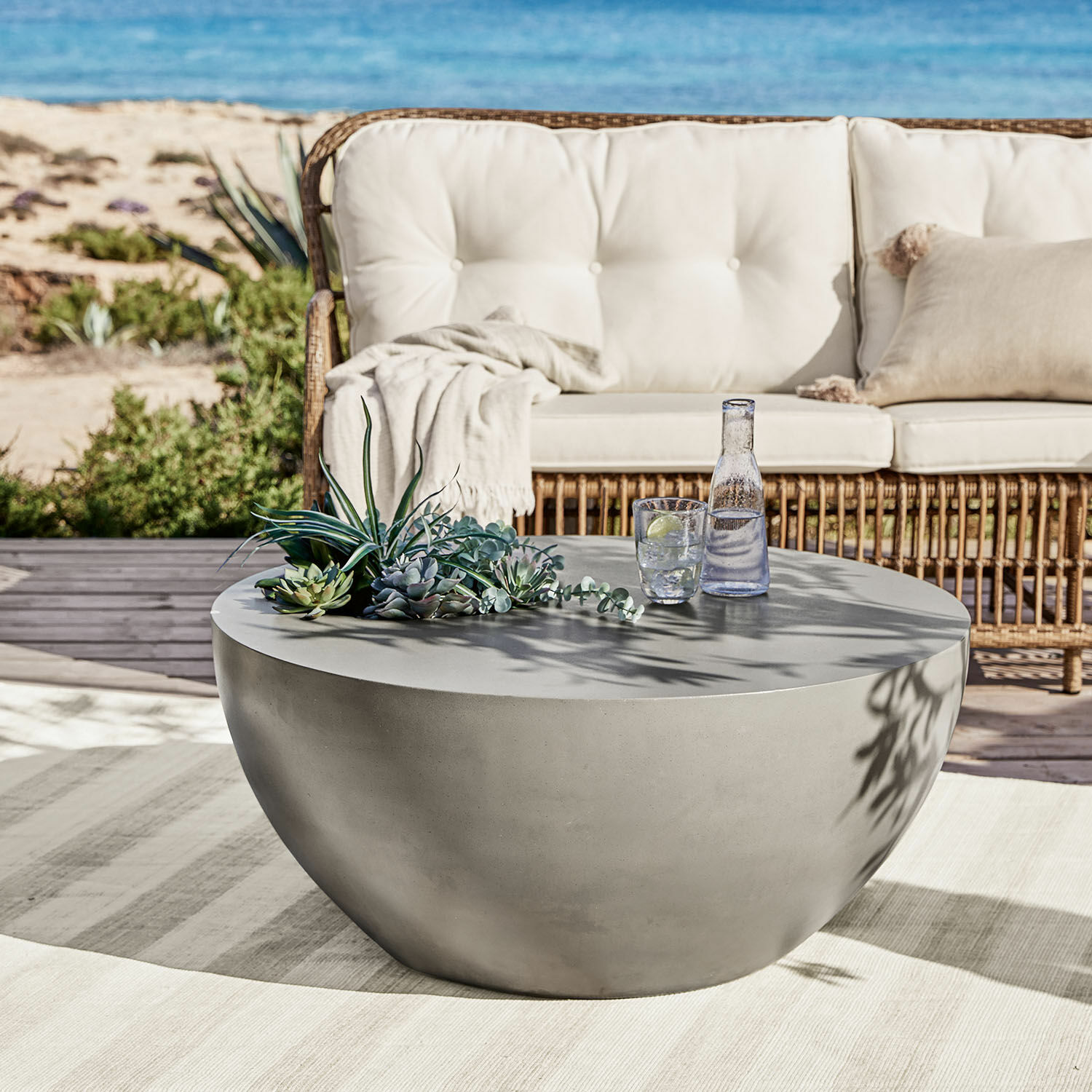 Mesa de centro Plévin Mesa de centro redonda gris de hormigón en terraza con decoración de suculentas y vaso de agua