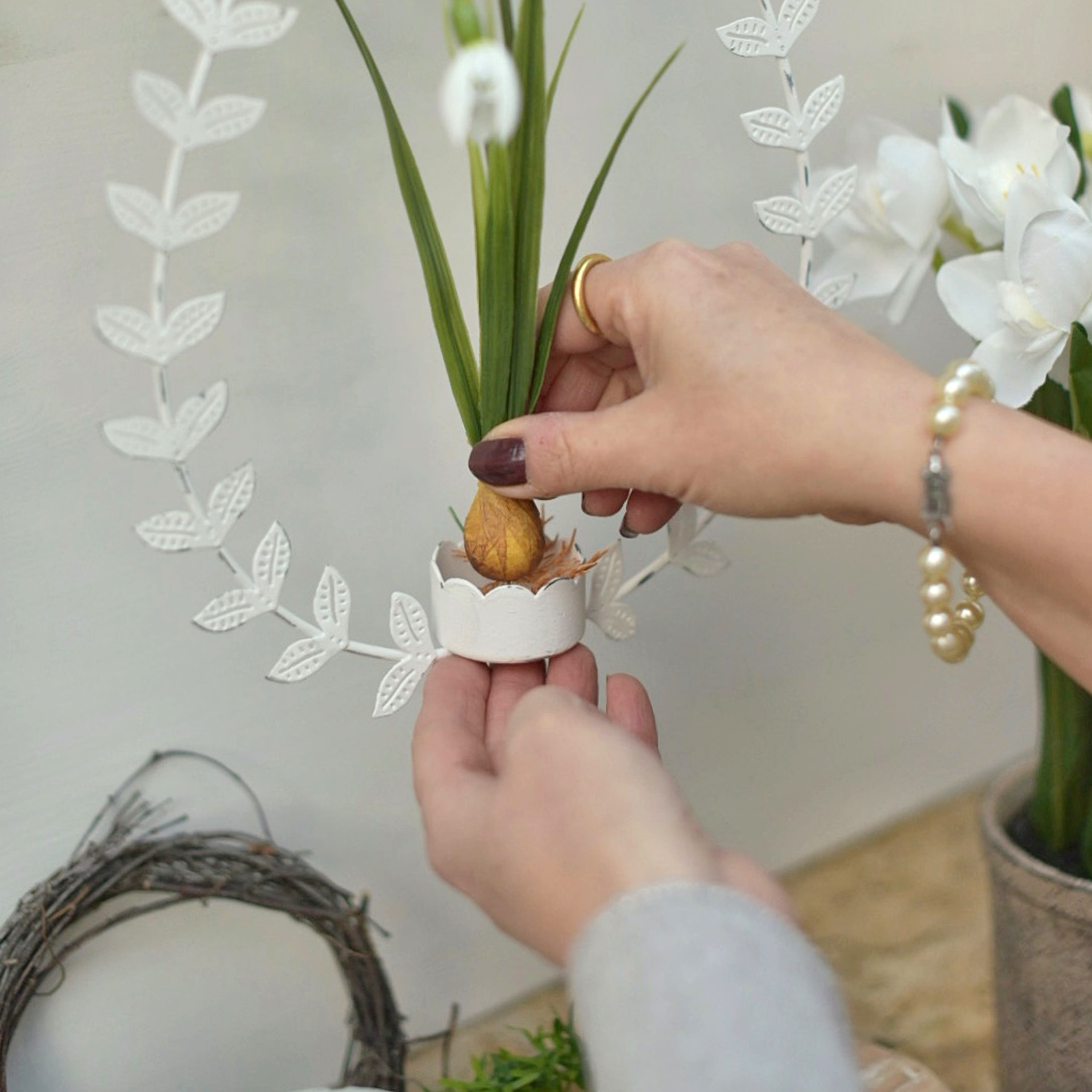 Manos colocando flor artificial en decoración metálica blanca con hojas para Pascua